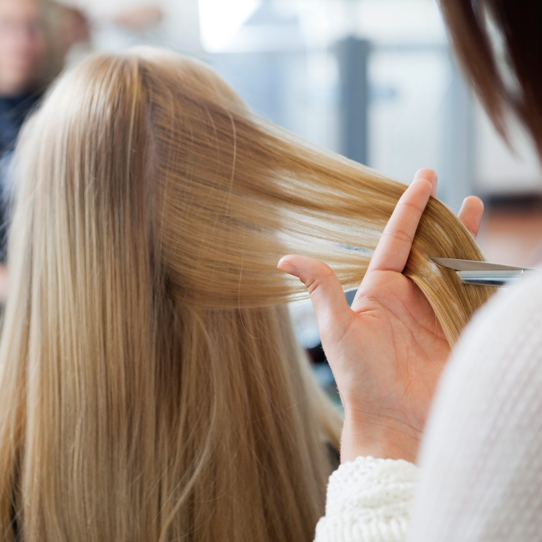 Hairdresser cutting blonde hair with scissors in salon.