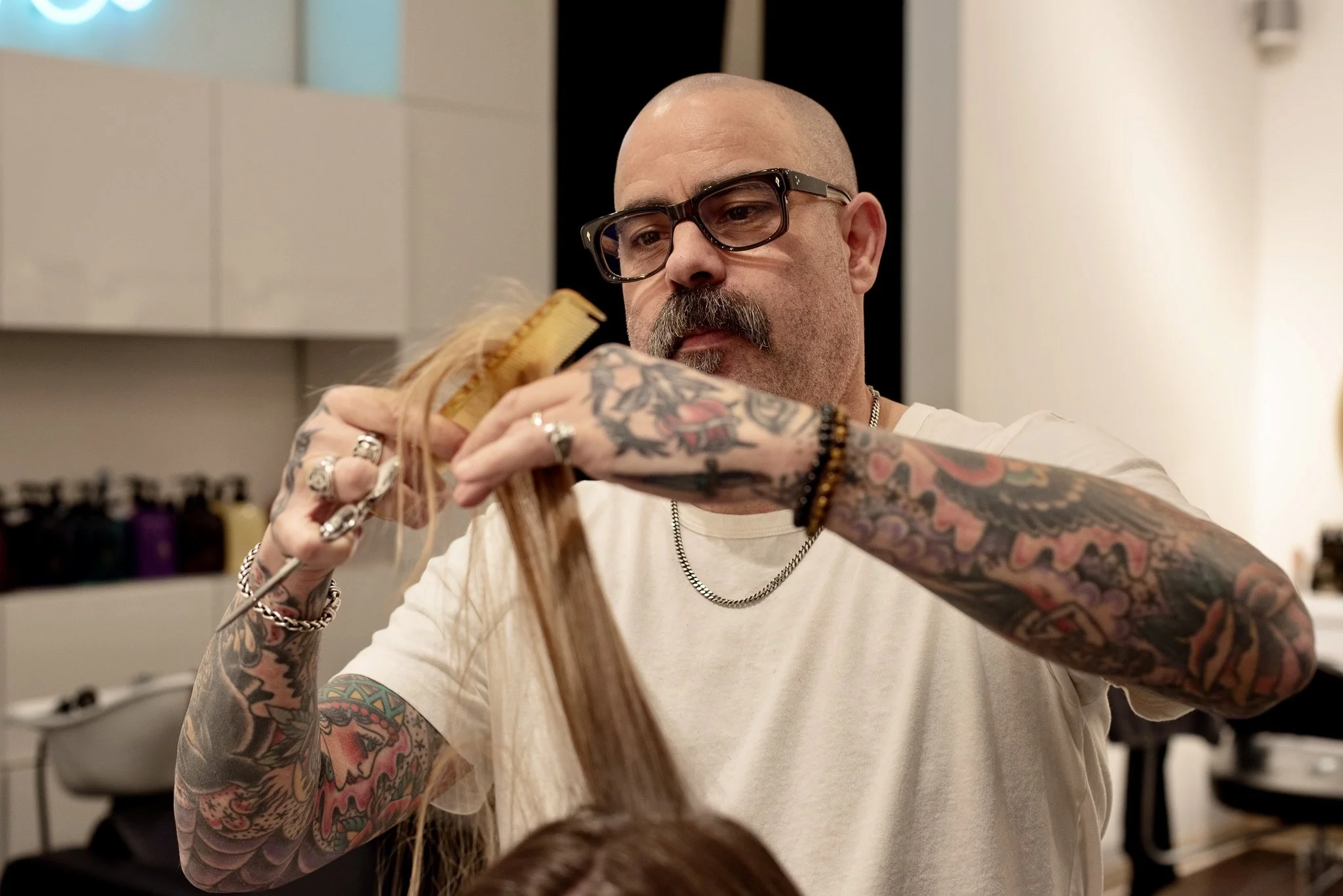 Tattooed hairdresser holding a hair extension or wig in a salon.