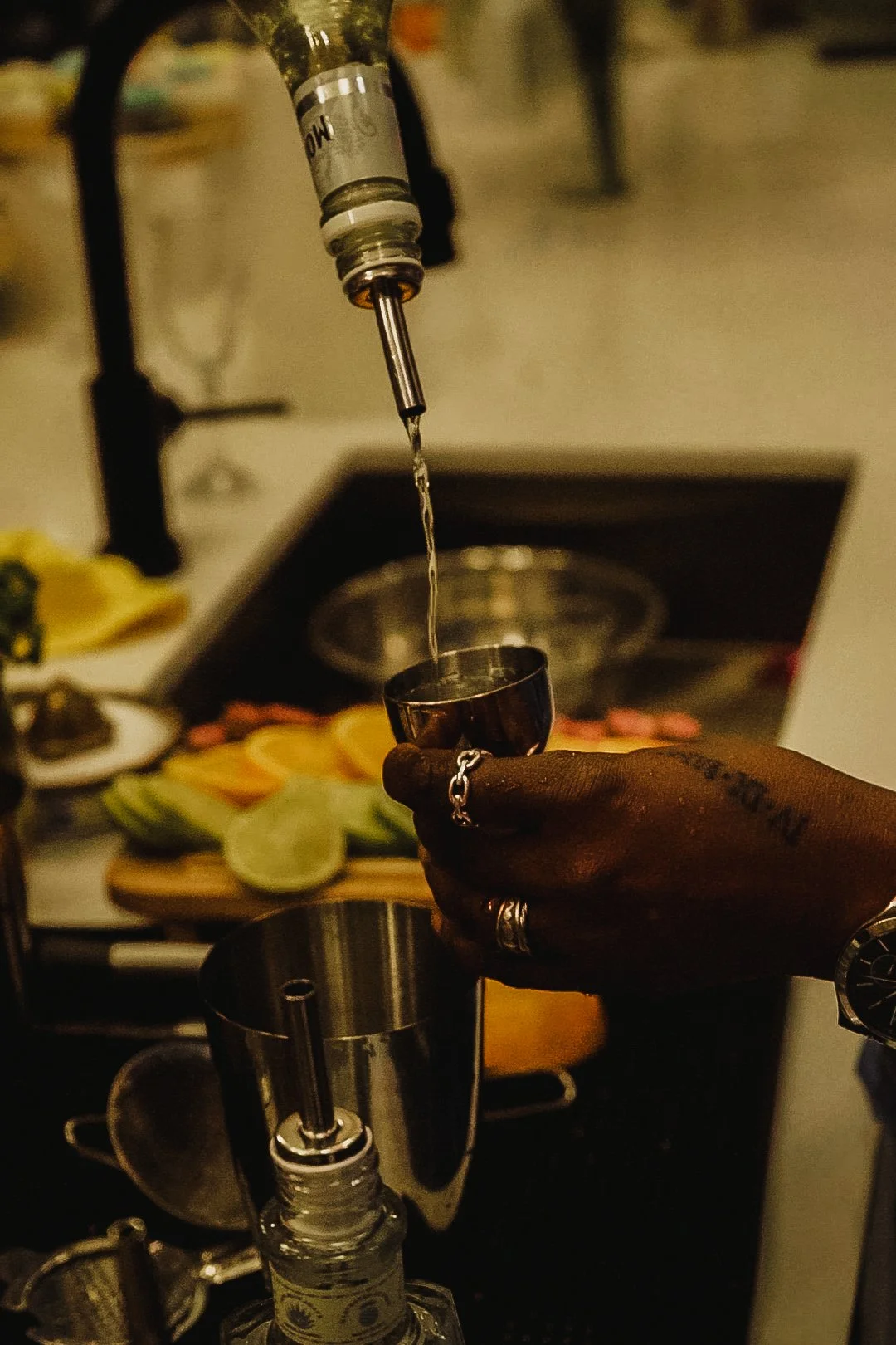Person pouring a clear liquid from a syringe into a small metal measuring cup, with sliced fruit visible in the background.