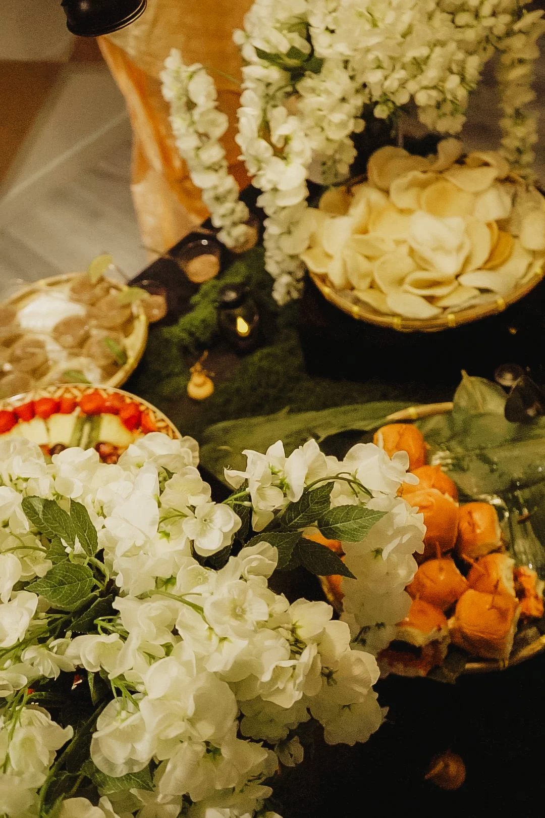 Table with white and orange flowers, bowls of chips, and an assortment of snacks.