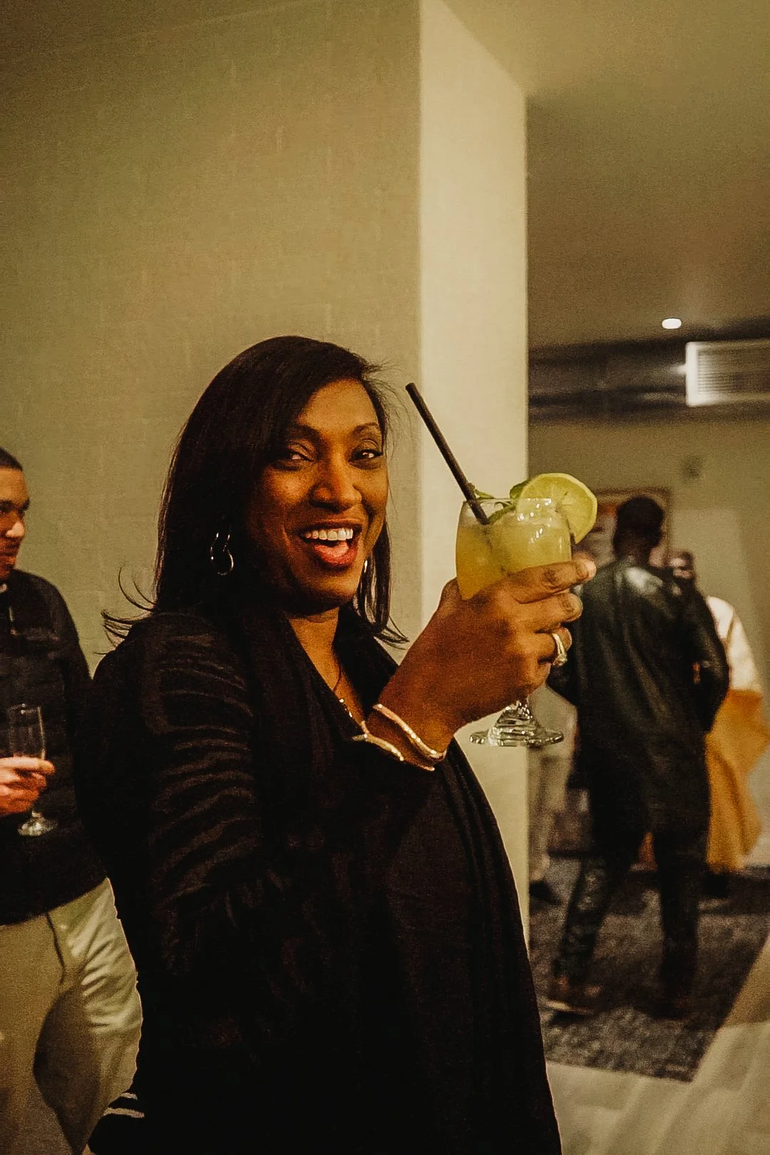 Woman smiling and holding a cocktail glass with lime, at a social event.