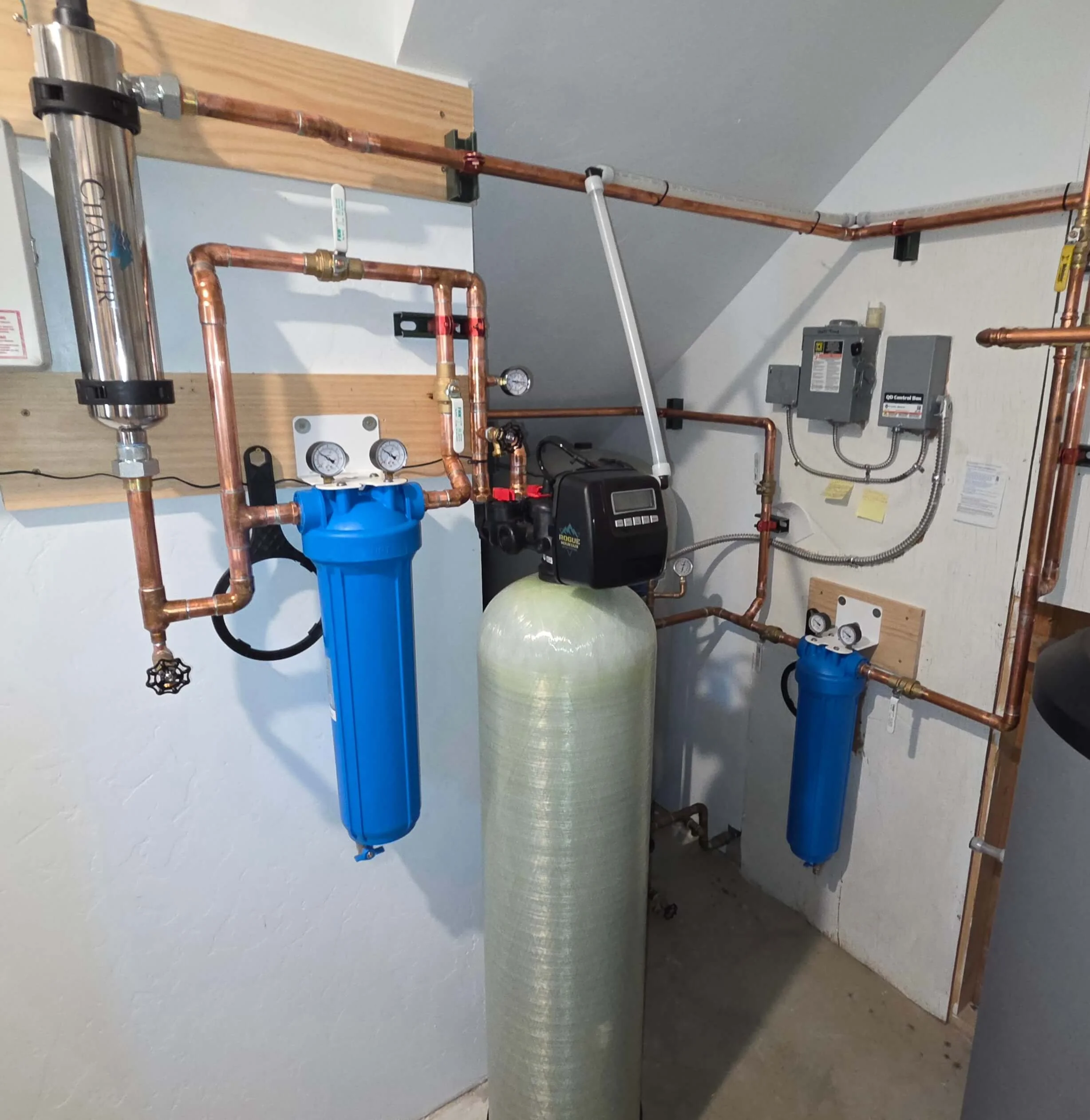 Interior view of a plumbing system with copper pipes, a water filter, pressure gauges, and an expansion tank mounted on a wall.