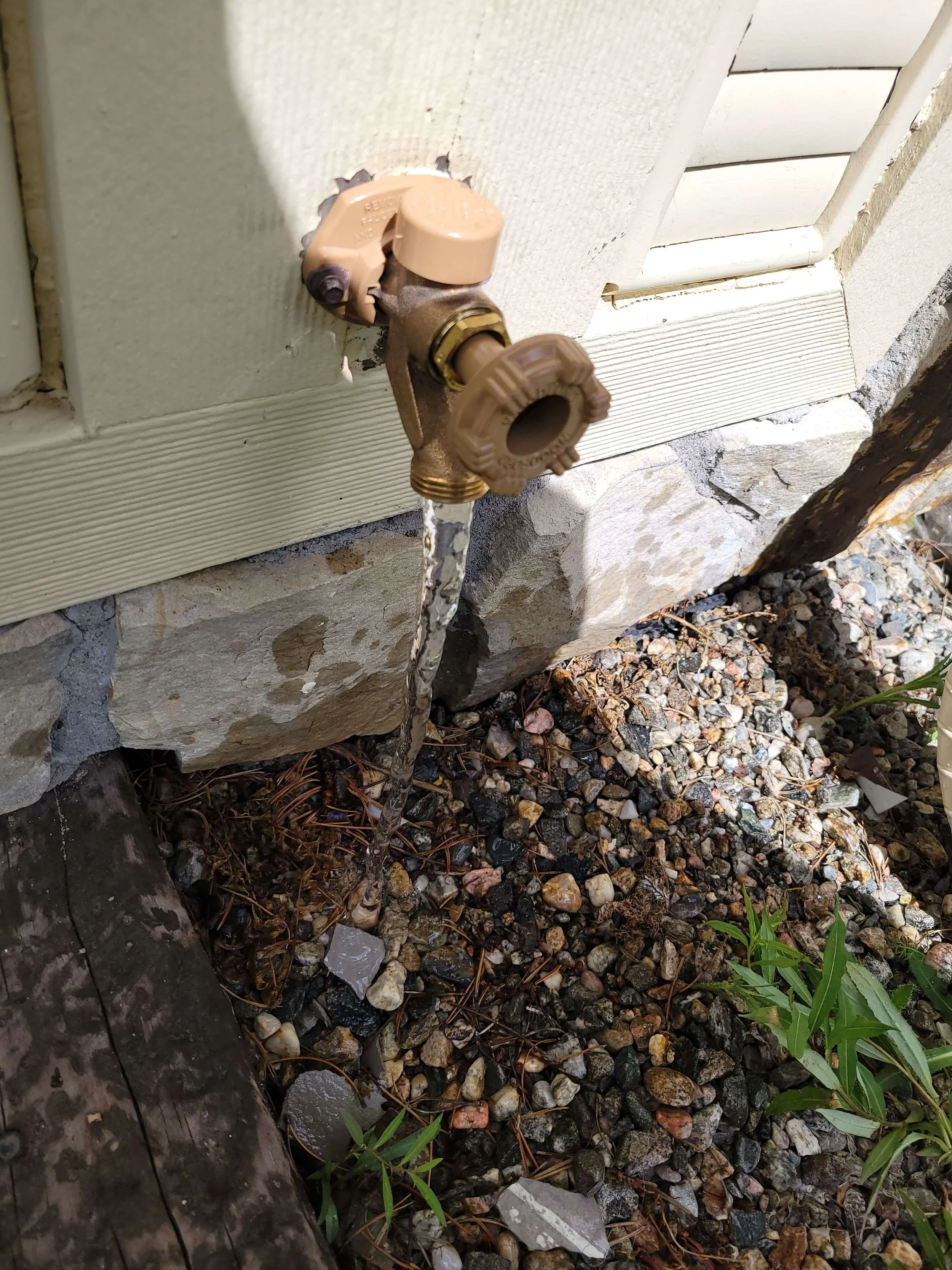 Outdoor faucet leaking water onto rocky ground beneath it.