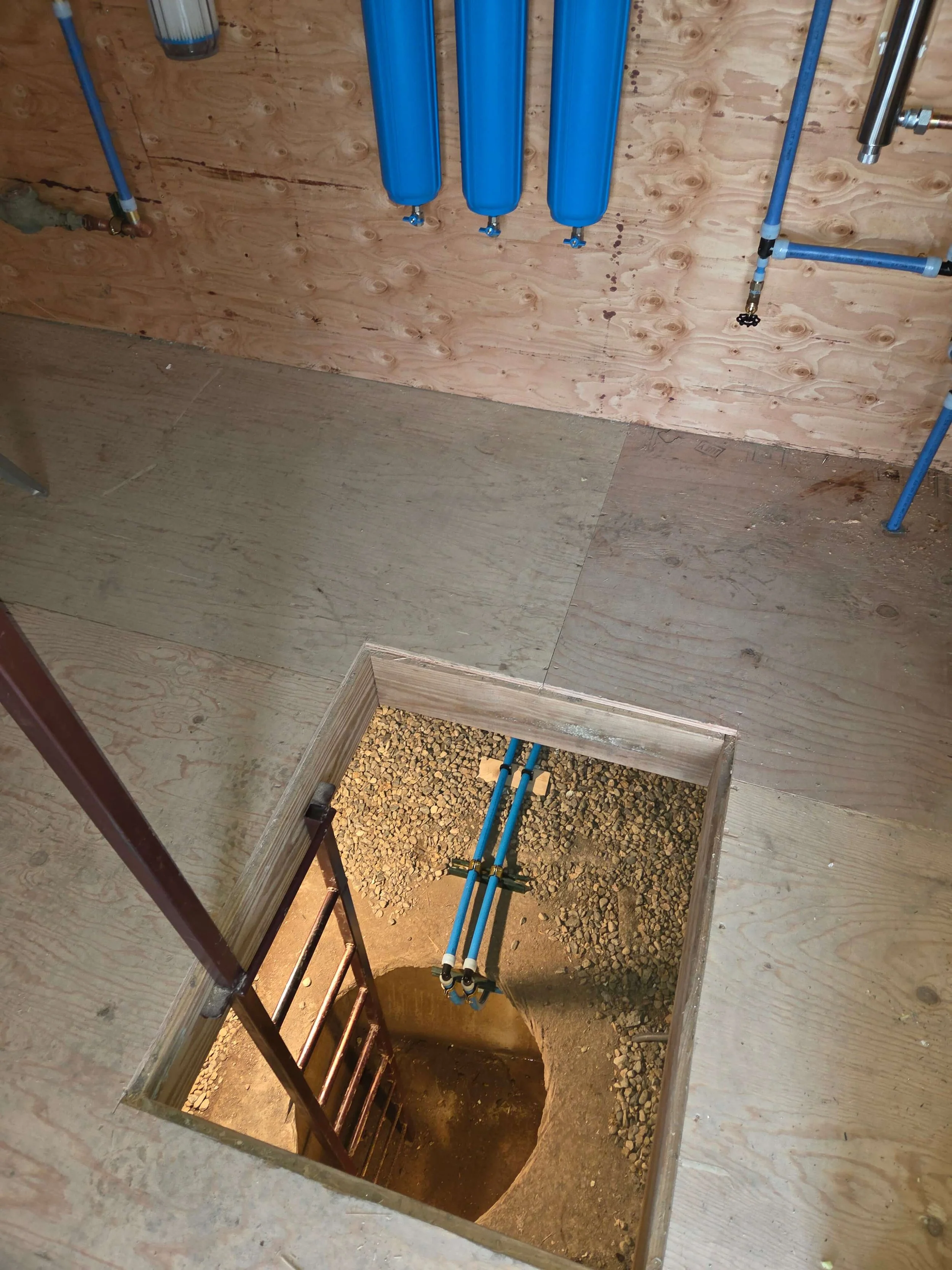 Construction site with plumbing pipes and an open hole in the floor leading to a staircase.