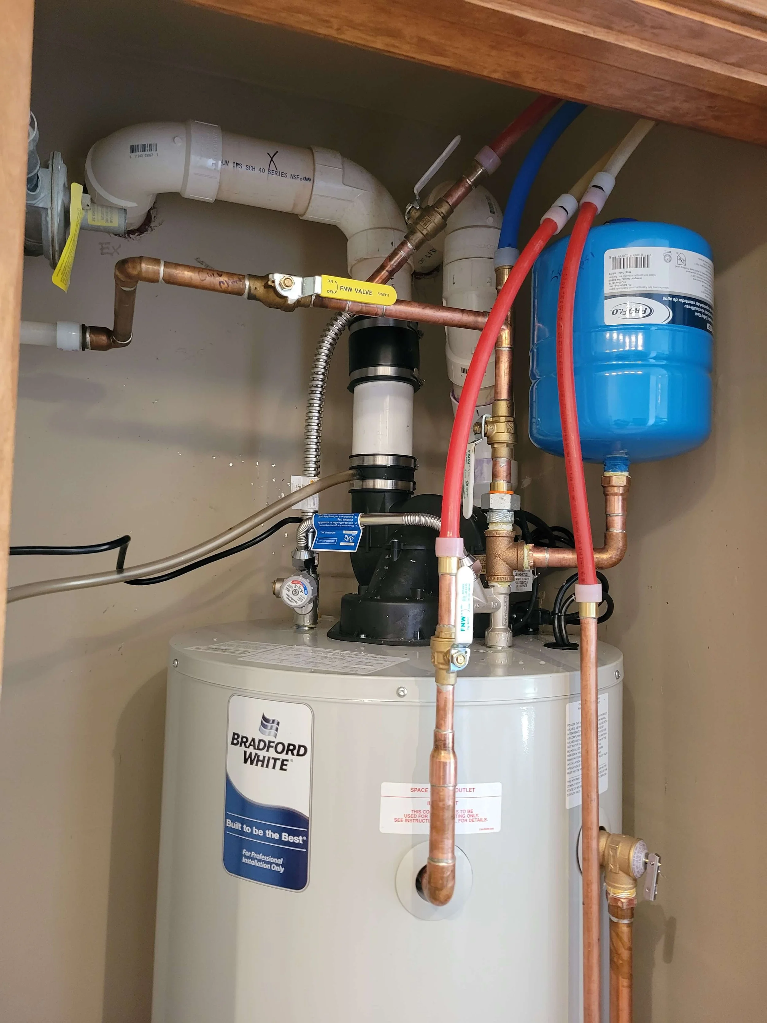 Water heater with pipes and expansion tank in a utility room, featuring copper and PVC connections.