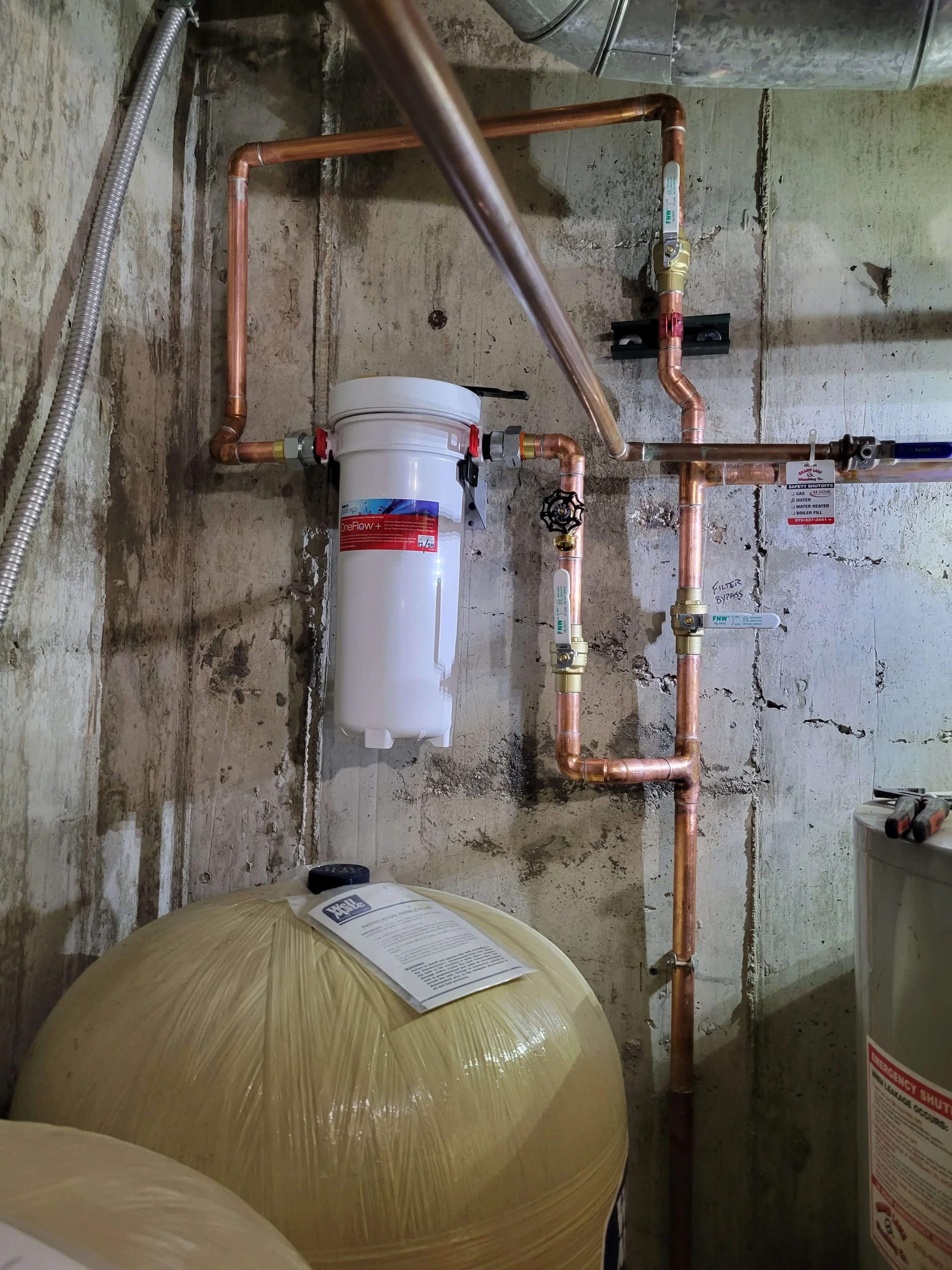 Water filtration system with copper pipes and tanks in a basement setting.