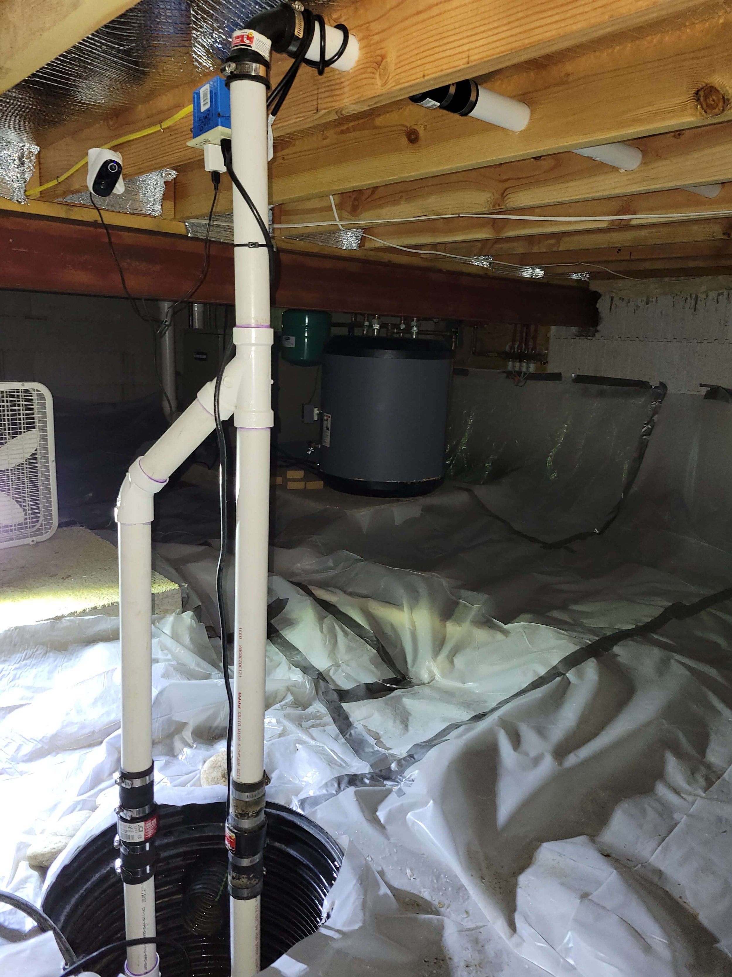 Crawl space with a sump pump system and white plastic vapor barrier covering the floor.