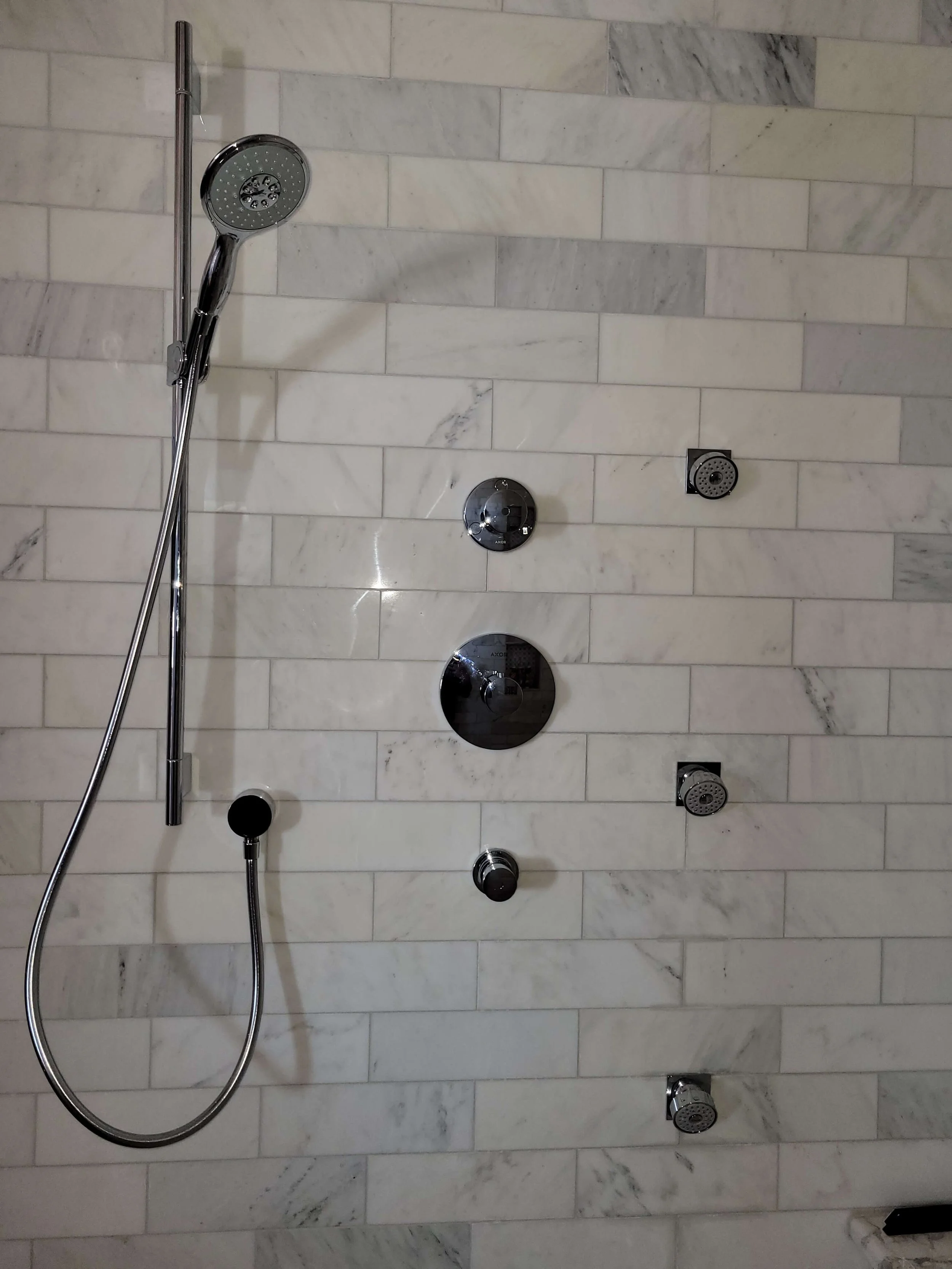 Luxury shower with white marble tile, adjustable hand shower, and multiple showerheads