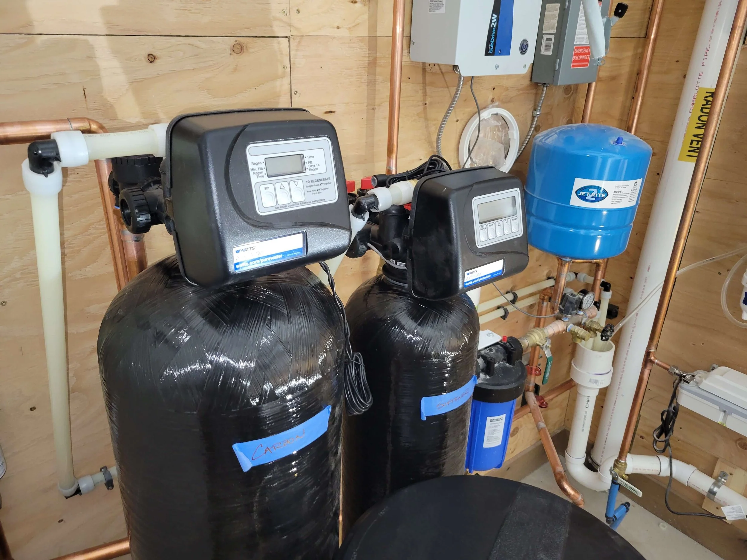 Water softener system with two large black tanks and control panels, blue pressure tank, and copper pipes.
