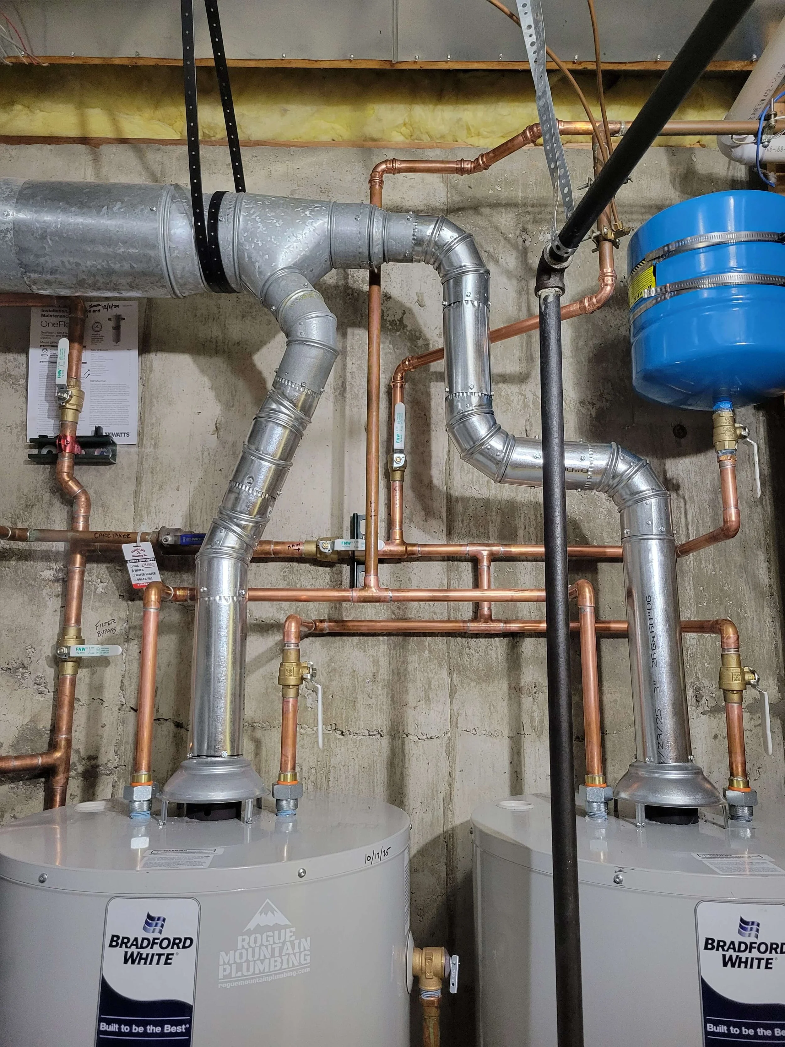 Two Bradford White water heaters connected to copper and metal pipes in a basement utility area.