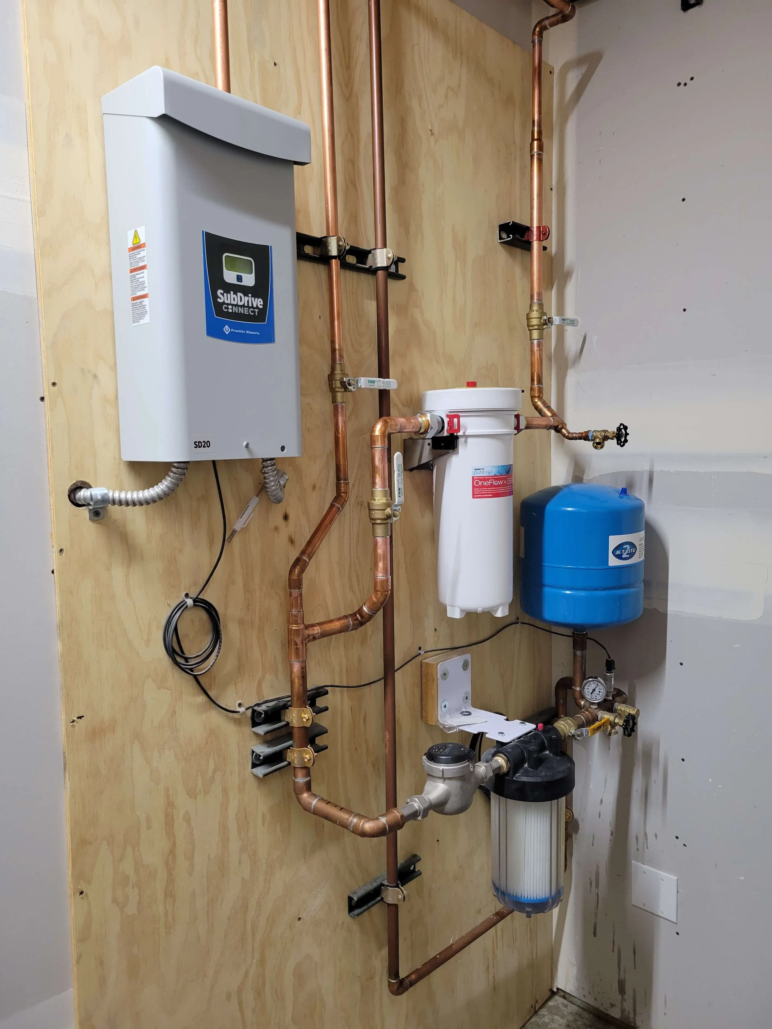 Water filtration and pressure system installation with pipes, filters, and control unit mounted on a wooden panel.