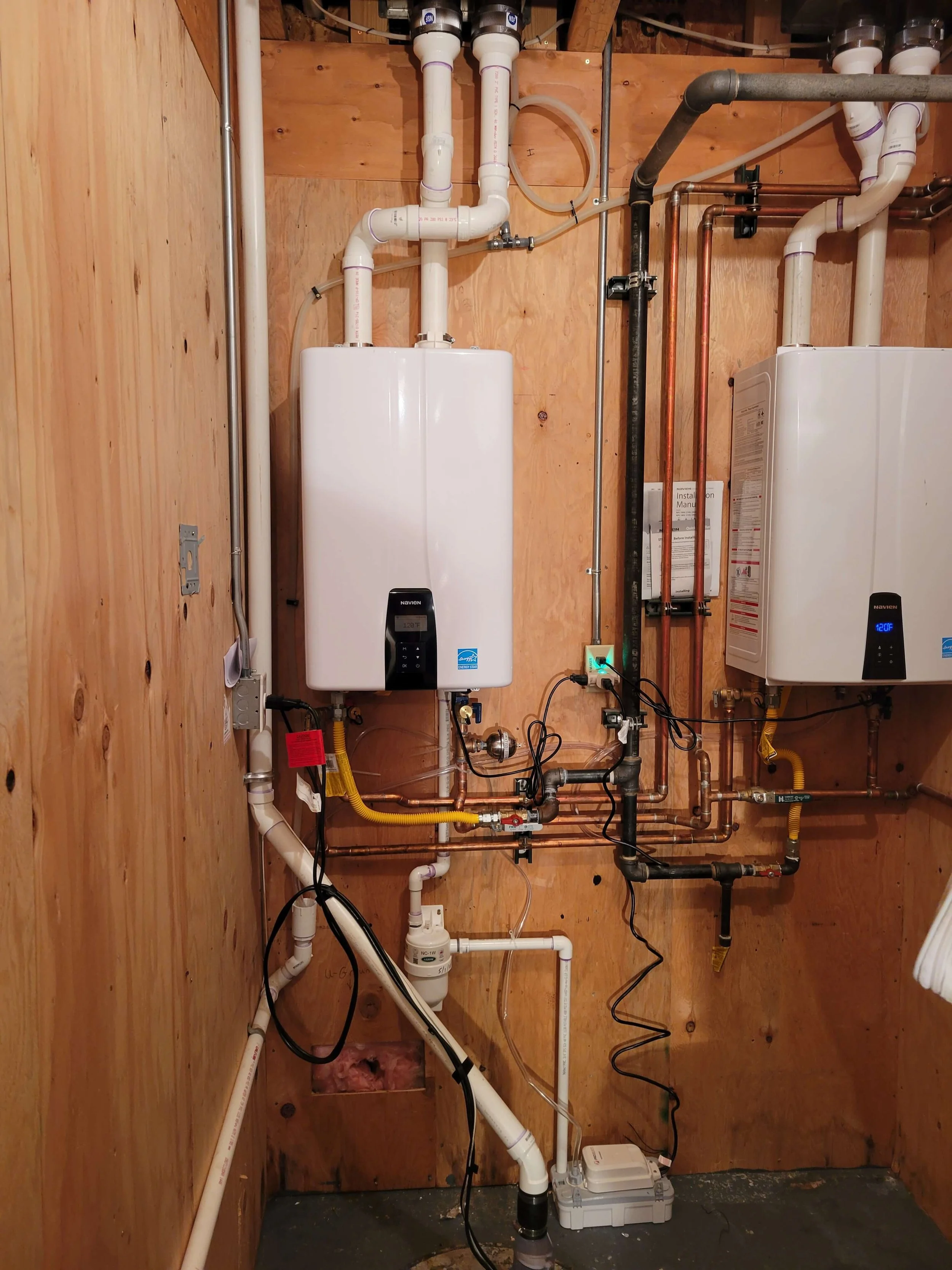 Basement installation of two tankless water heaters with pipes and wiring.