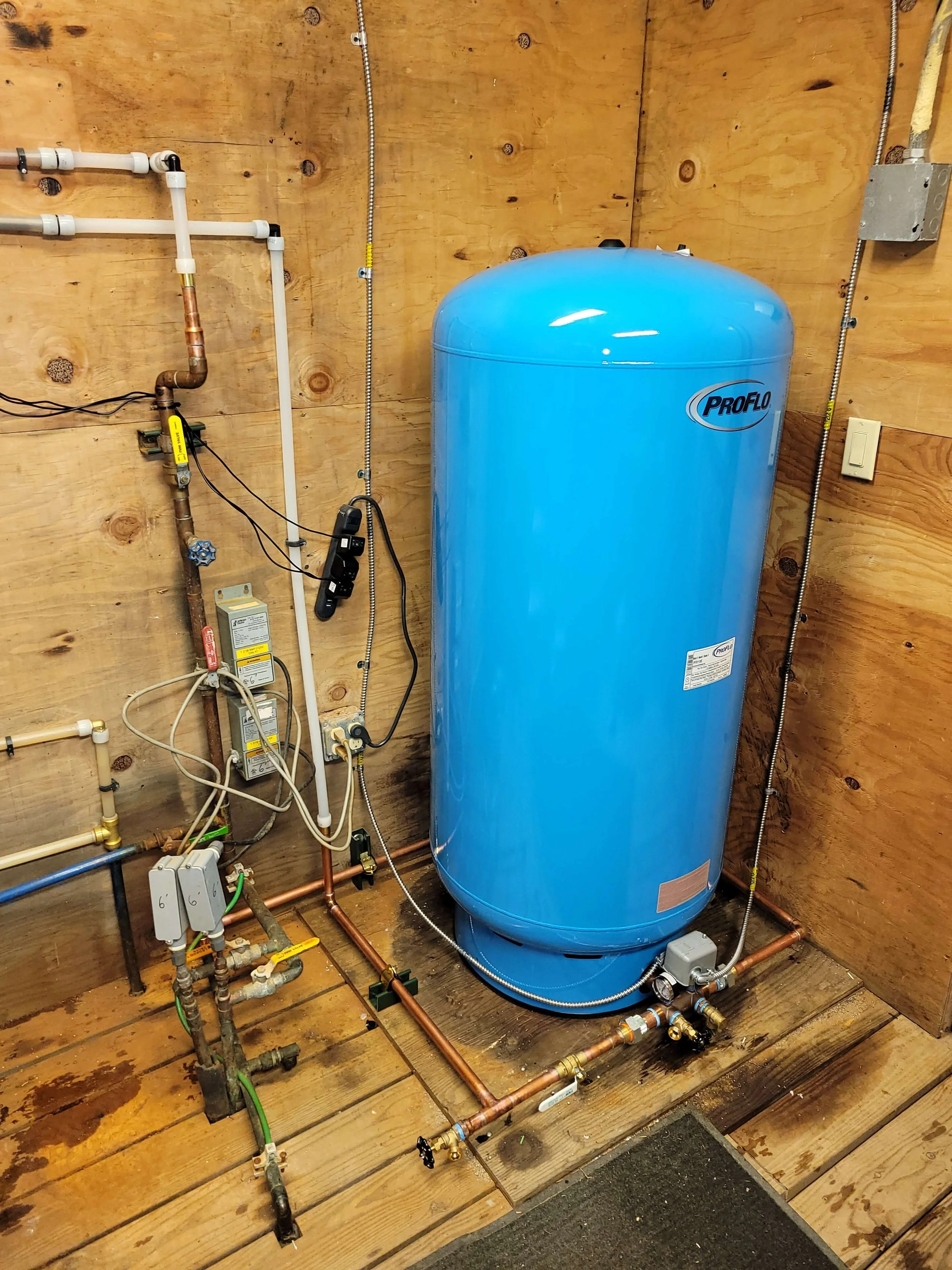 Blue pressure tank installed in a wooden utility room with connected pipes and electrical wiring.