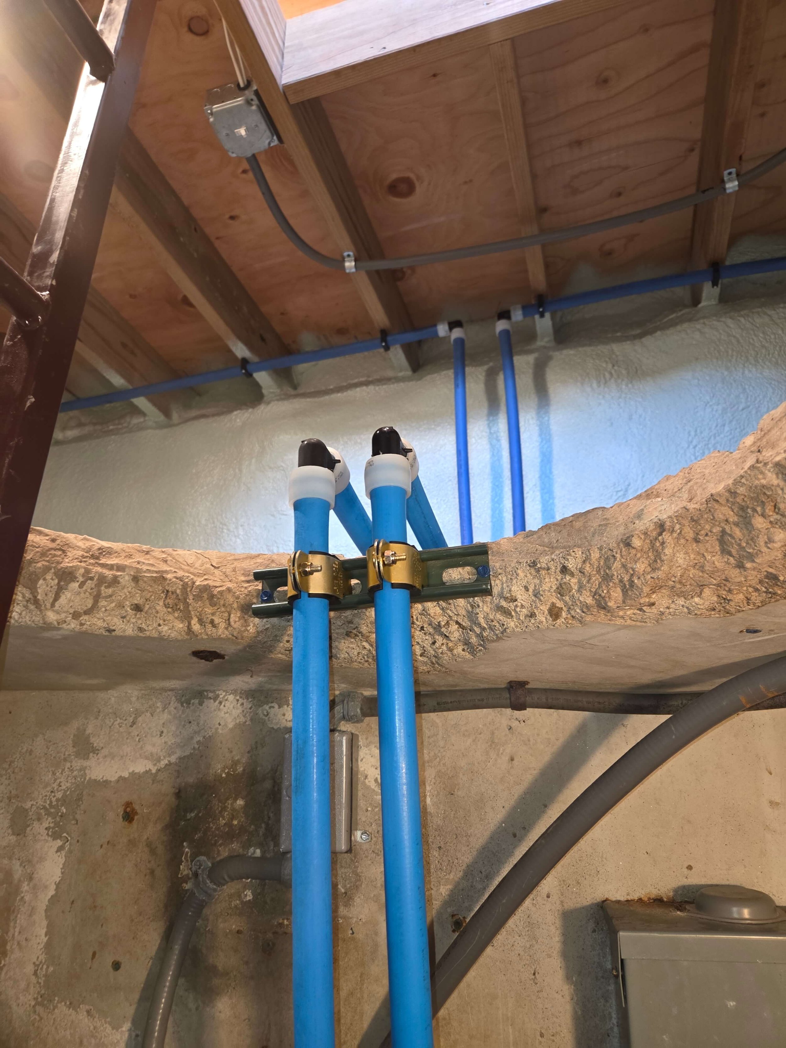 Plumbing pipes and electrical wiring installed on a ceiling and wall in an unfinished area.