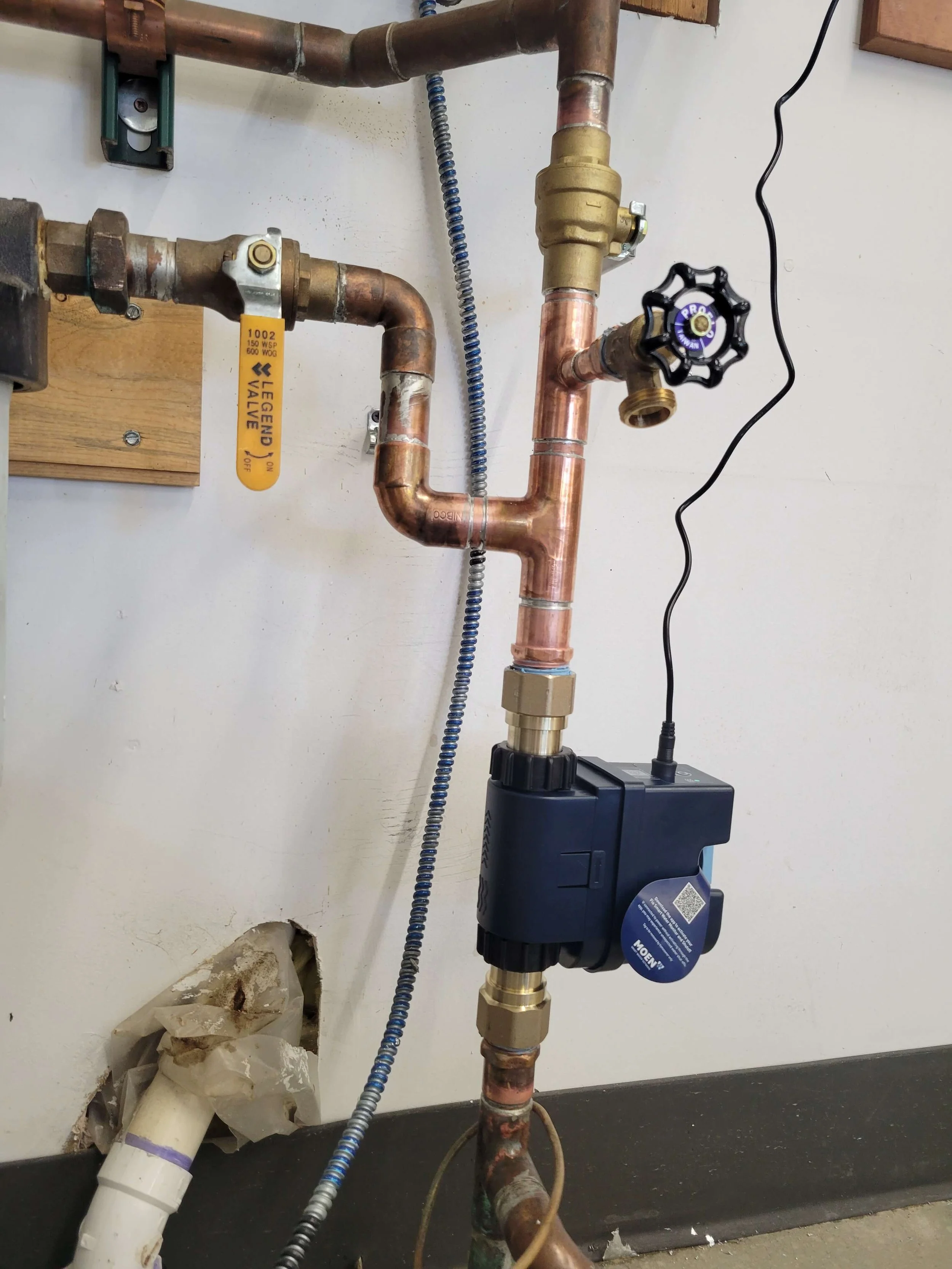 Plumbing pipes with valves and a connected digital flow meter on a wall.