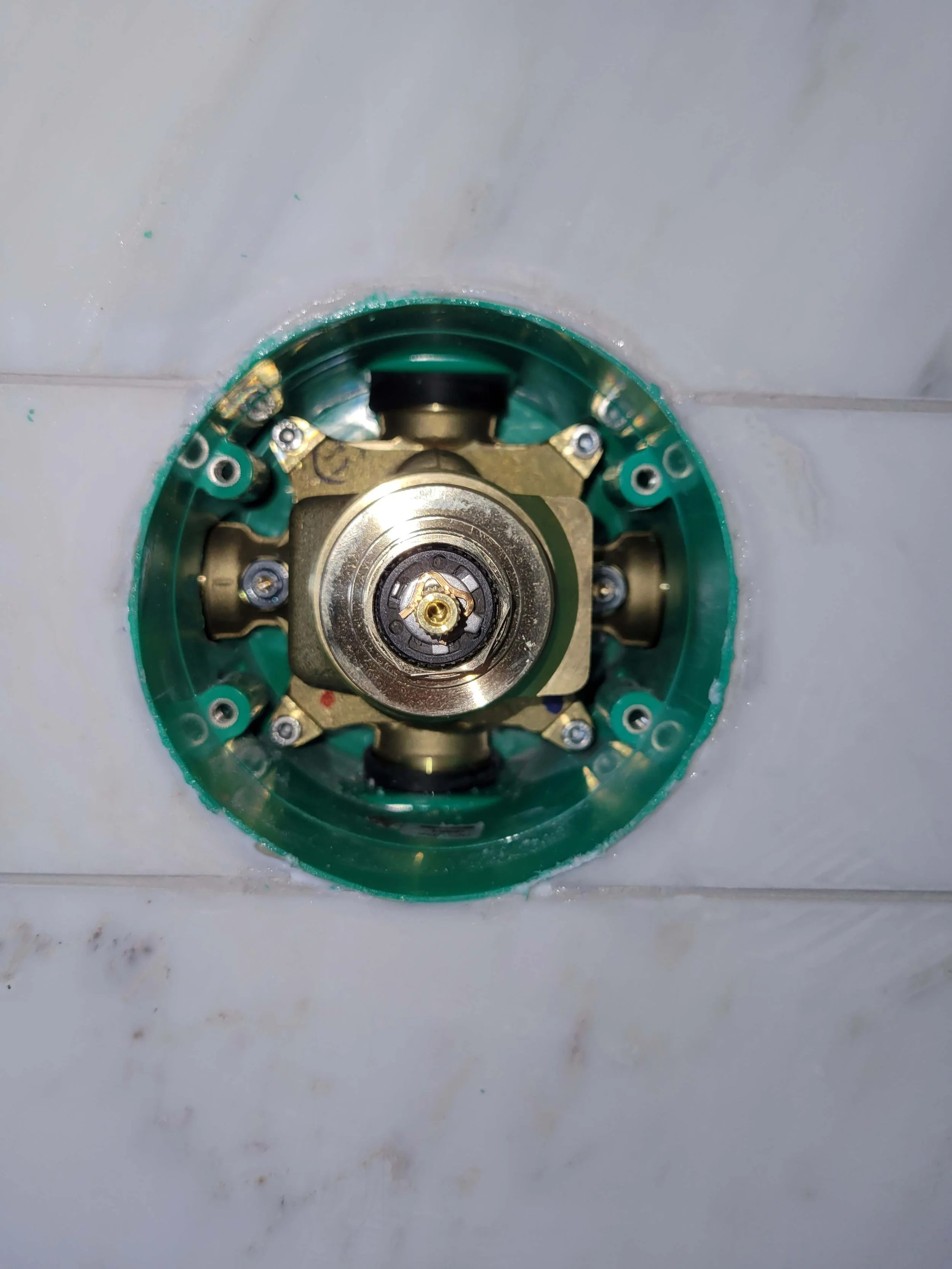 Close-up of a brass shower valve inside a green plastic housing, set into a tiled wall.