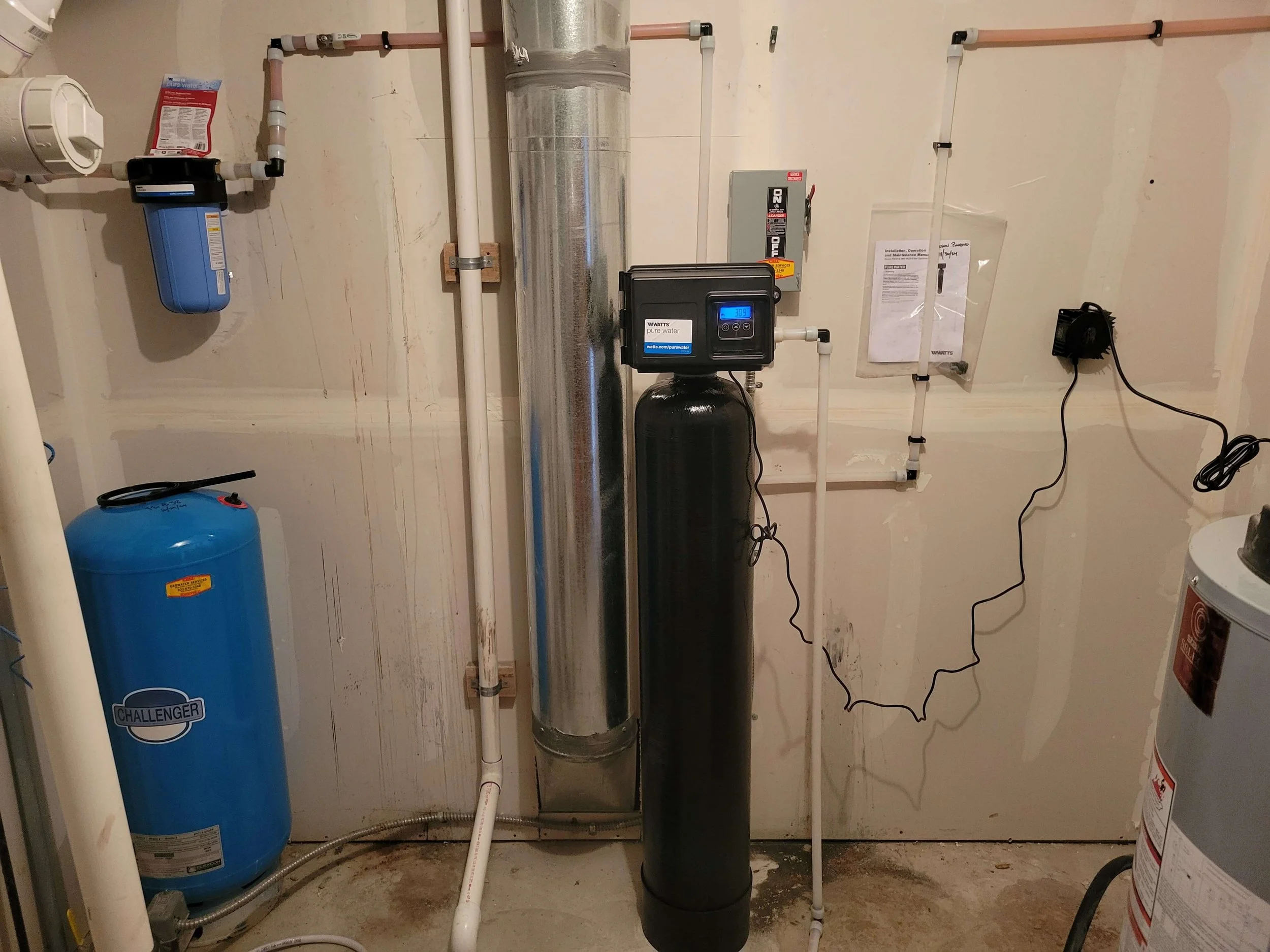 Basement water filtration and softener system with blue tank and pipes.