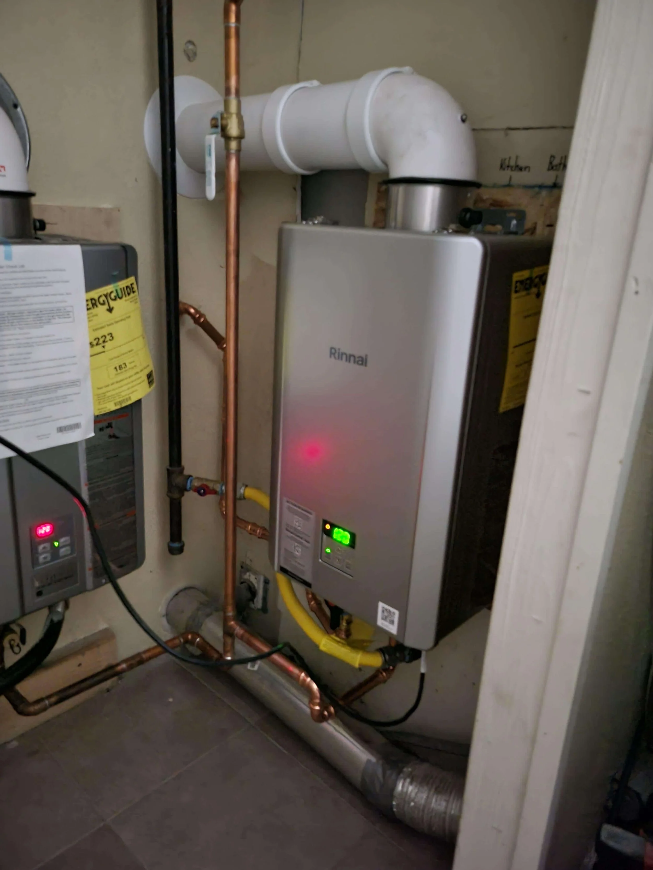 Tankless water heater system with pipes and ventilation in a utility room.