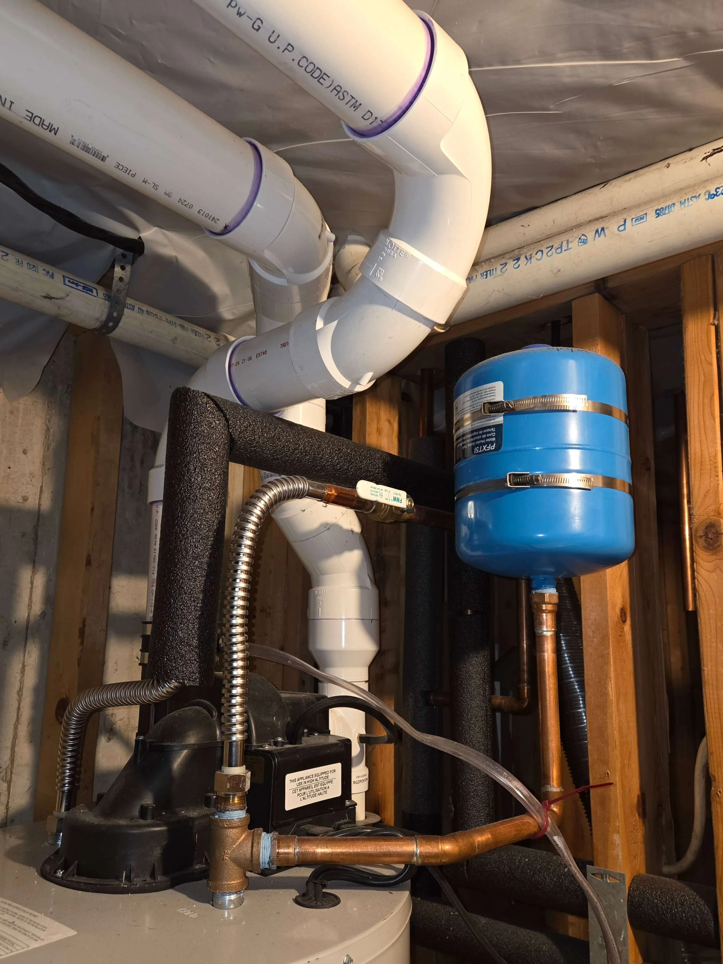 A sump pump system installed in a mechanical room with PVC piping, a blue pressure tank, and a submersible pump.