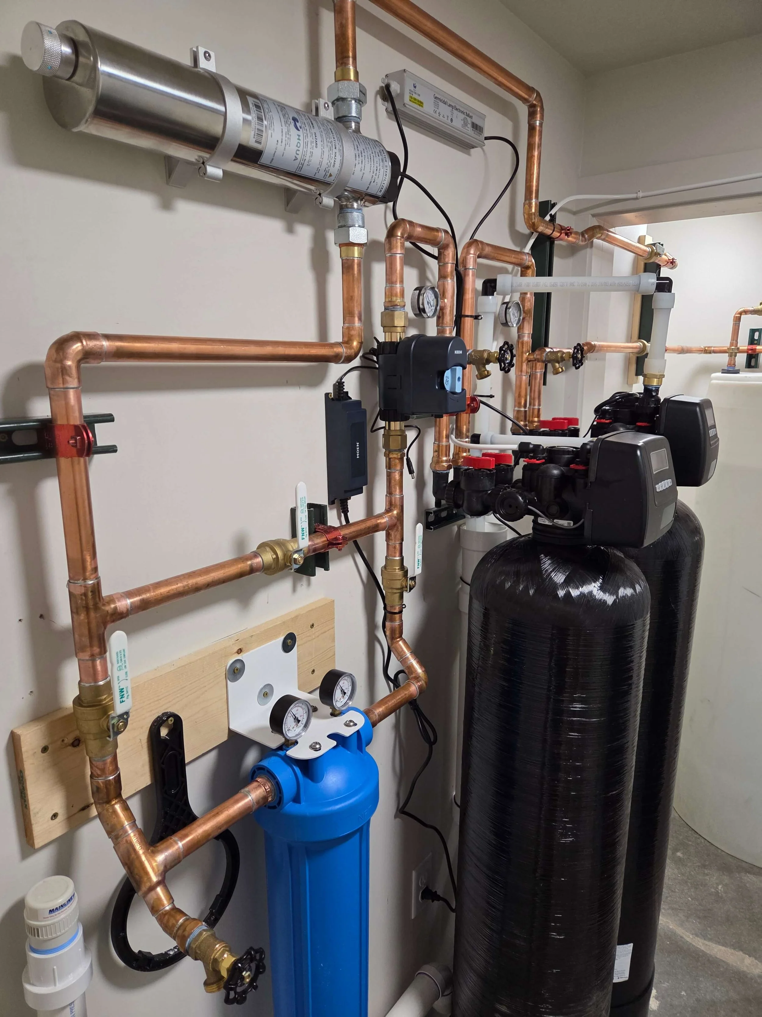 Plumbing system with copper pipes, a water filter, gauges, and a black water softener tank.