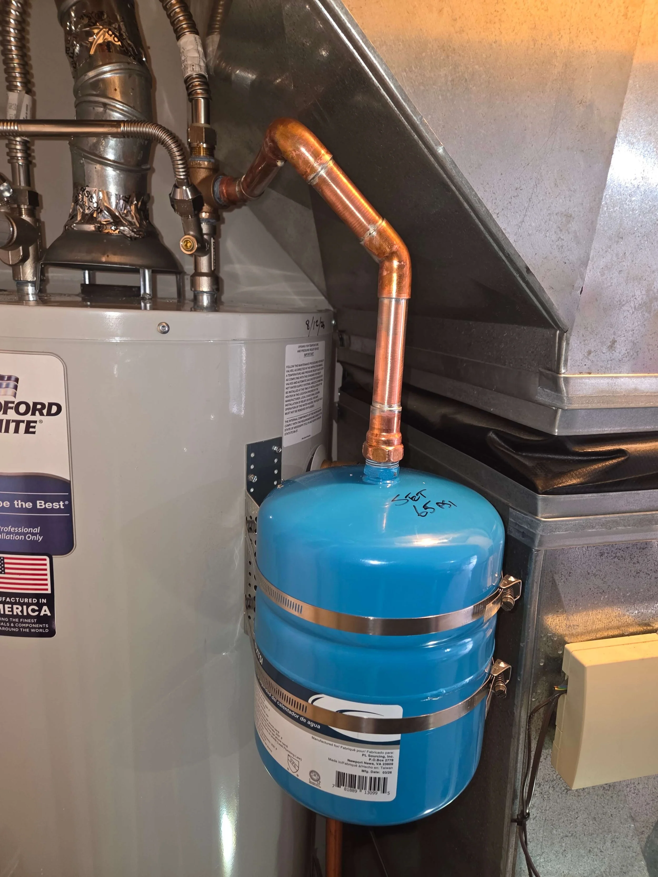 A water heater unit with copper pipes and a large blue water filter connected below it.