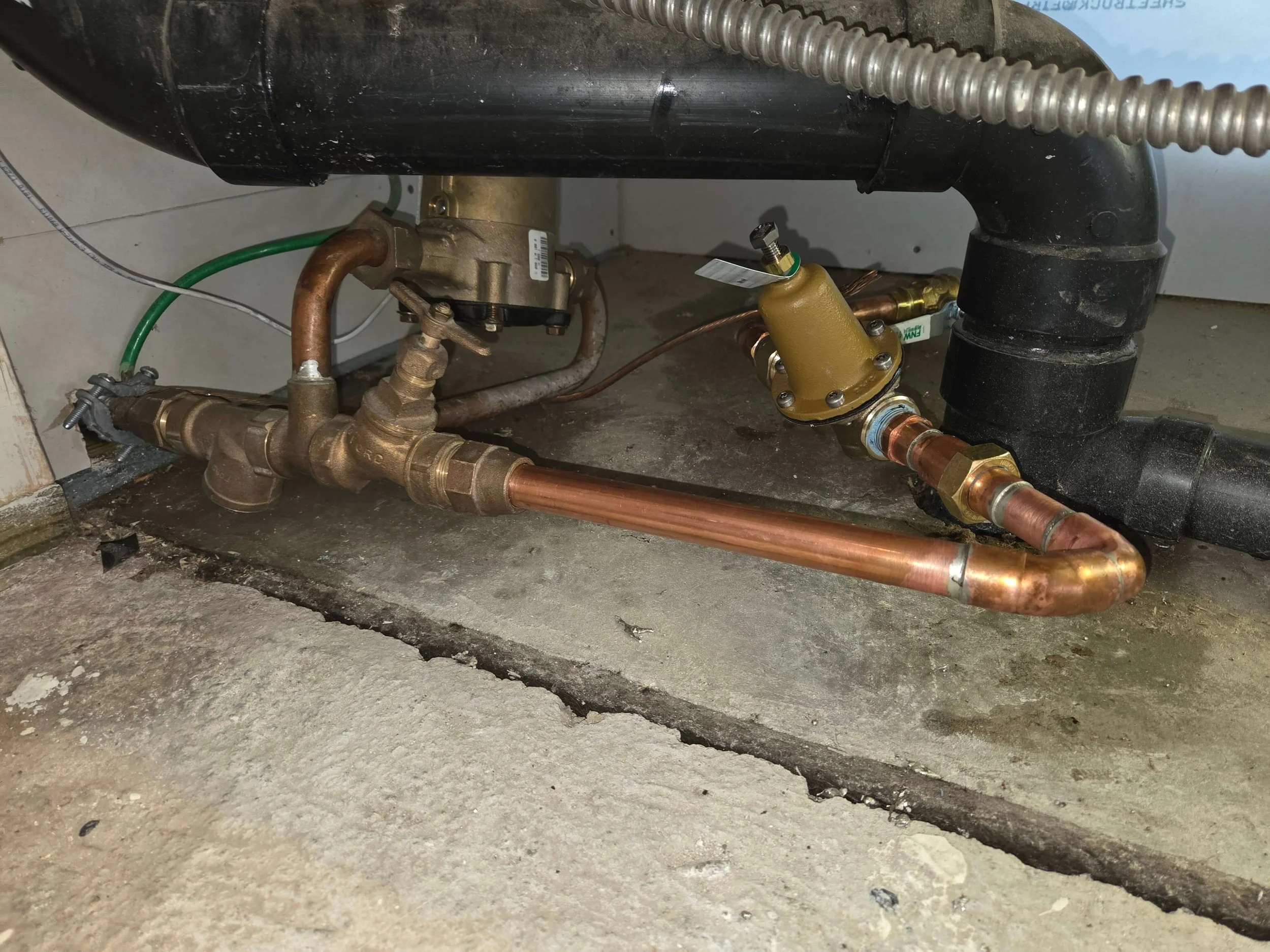 Underground plumbing system including copper pipes, valves, and a black pipe, with a concrete floor and trench for installation.