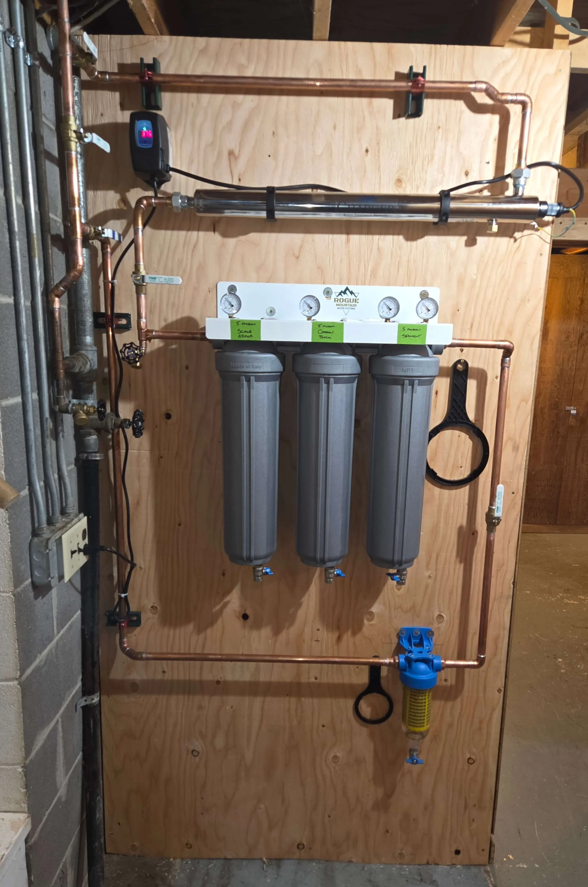 Plumbing system with copper pipes, gauges, water filters, and a water pressure regulator mounted on a wooden board.