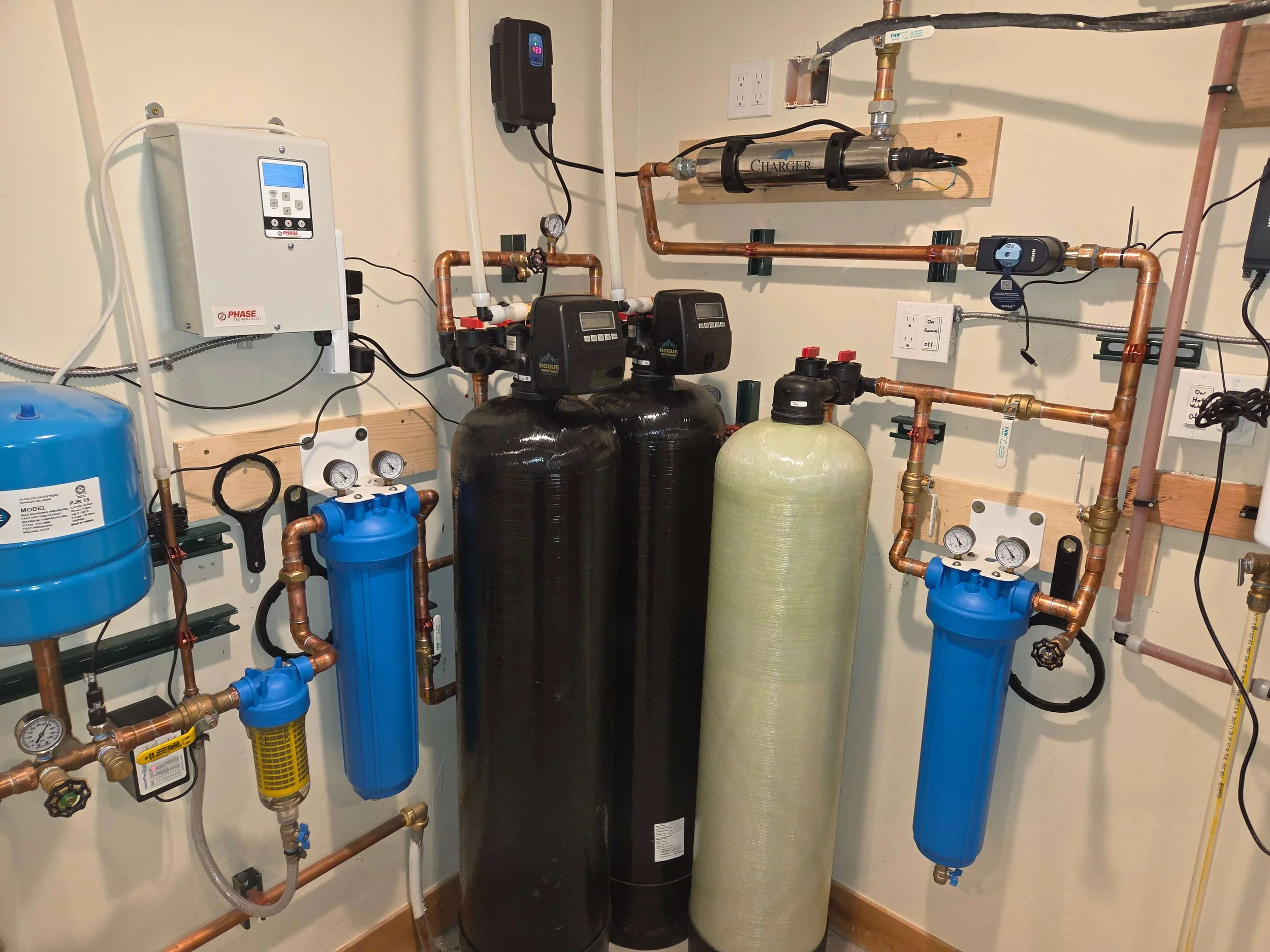 A utility water filtration and pressure system with various pipes, gauges, and tanks installed on a wall.
