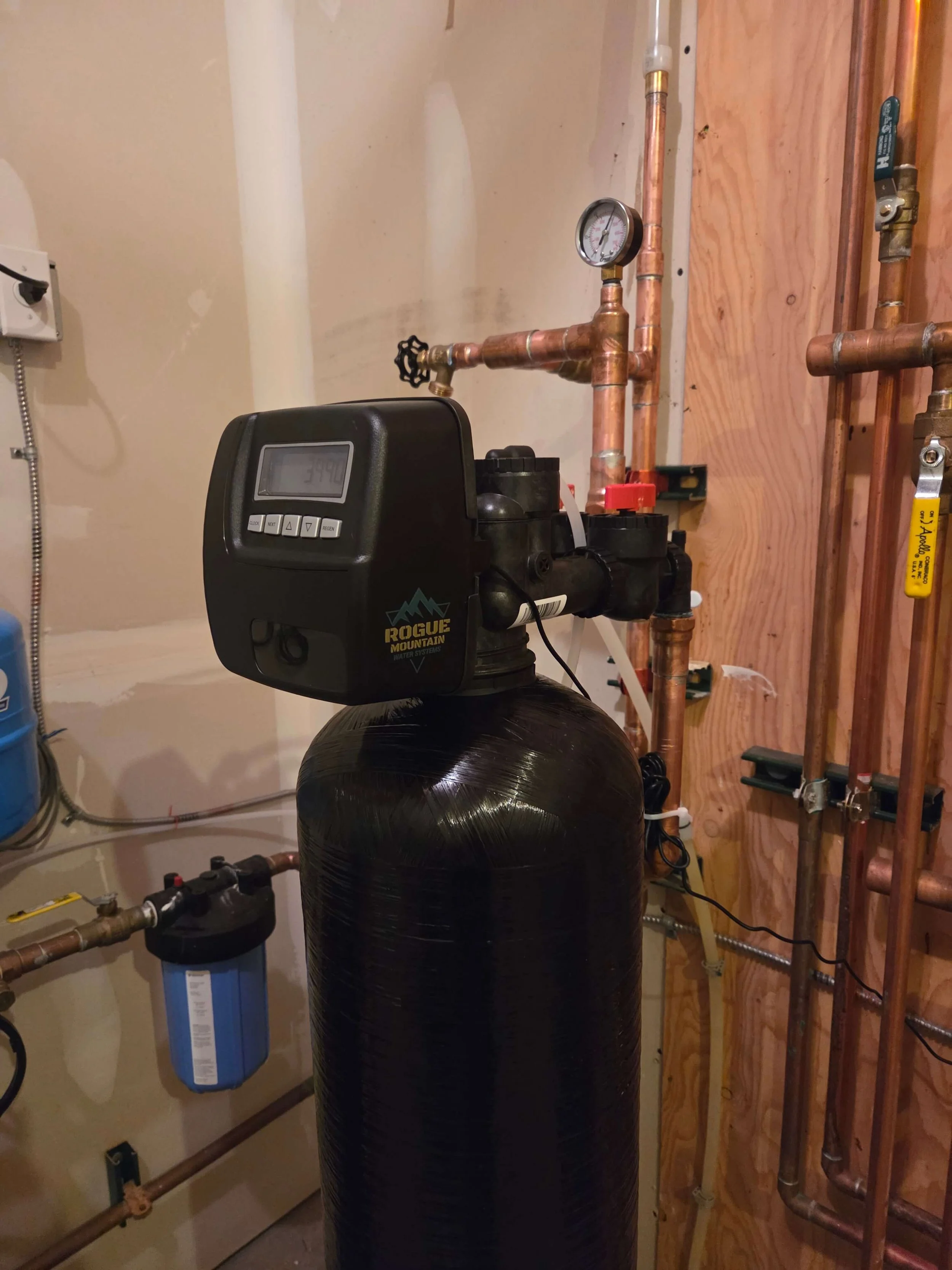 A water softener system in a basement utility room with copper pipes and a water filter.