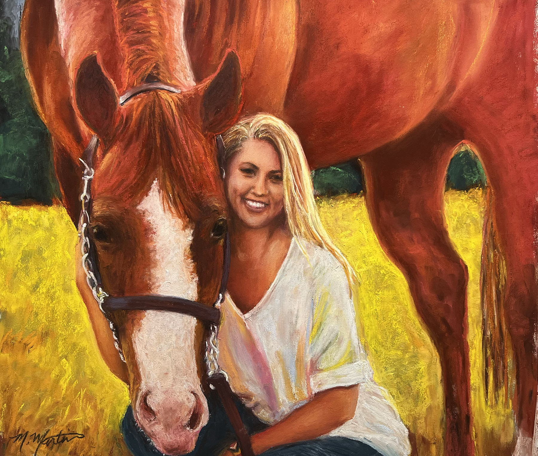 A woman with long blonde hair smiling and sitting next to a large brown horse with a white stripe on its face, in a field of yellow grass with trees in the background.
