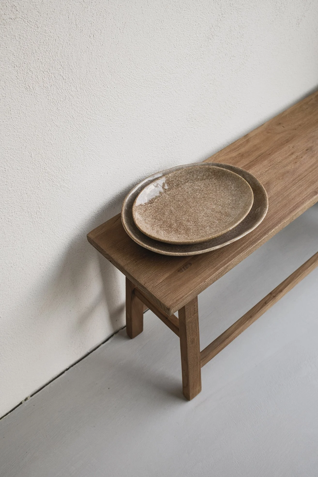 Two ceramic bowls stacked on a wooden bench against a white wall.