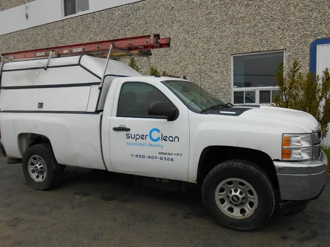 White service truck with ladder on top, parked outside a building, with branding for Super Clean Specialized Cleaning including a phone number.