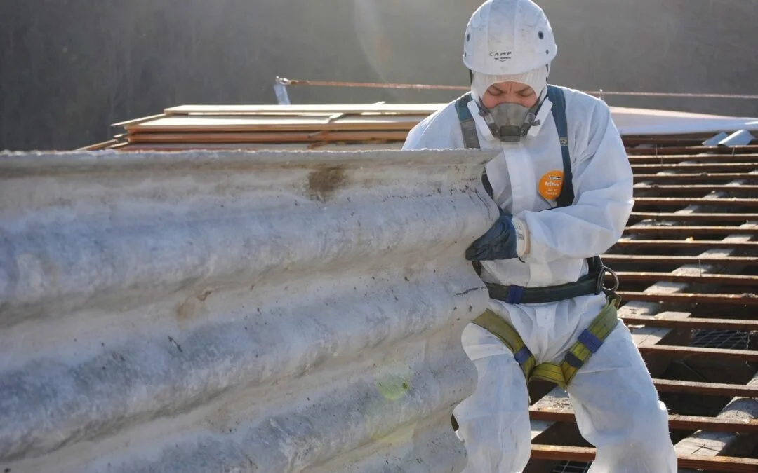 A worker in safety gear, mask, and gloves is installing or repairing a metal roof on a building.