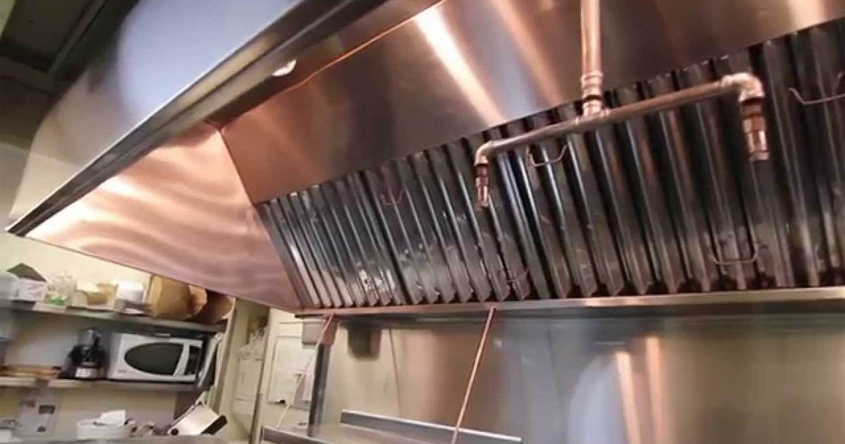 A commercial kitchen hood with grease filters and a sprinkler pipe underneath.