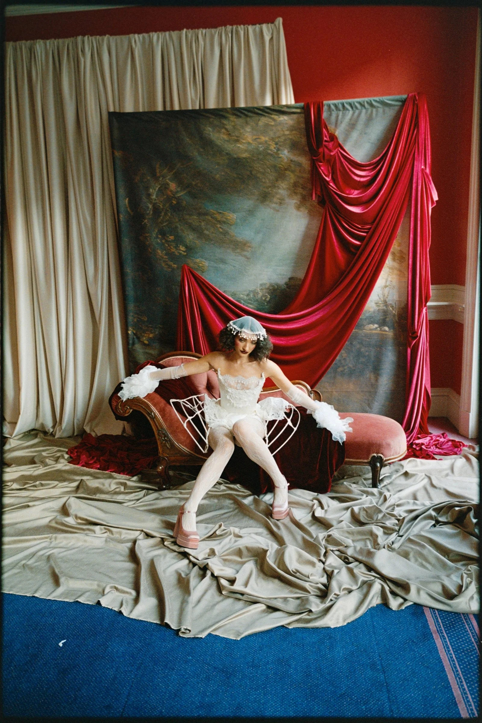 Female performer in a white gown seated within the red theatre set