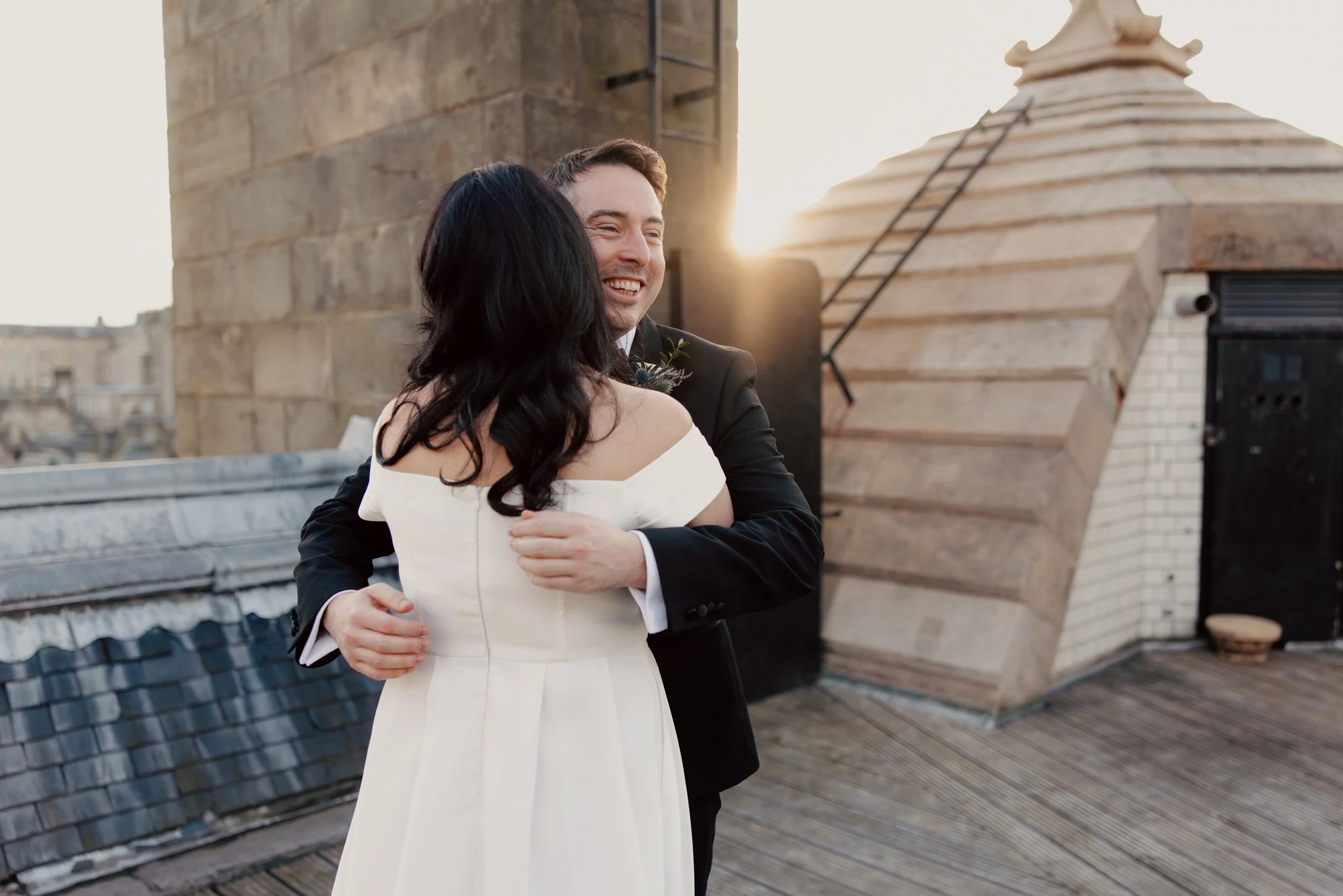 Milly and Vincent embracing on the rooftop in low winter sunlight.