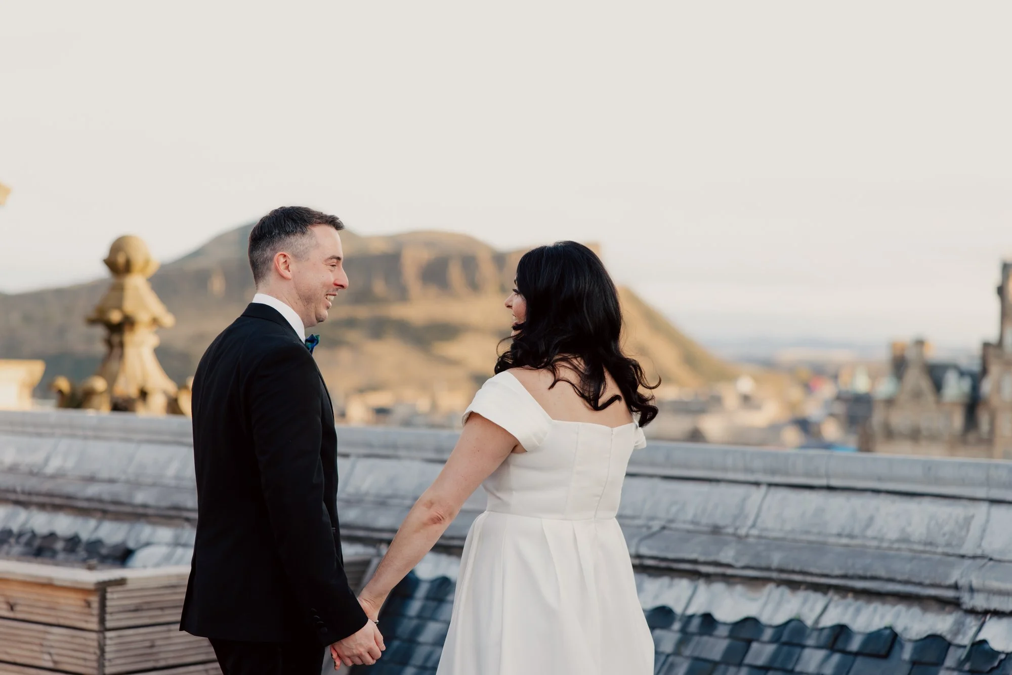 The couple holding hands with Edinburgh behind them.