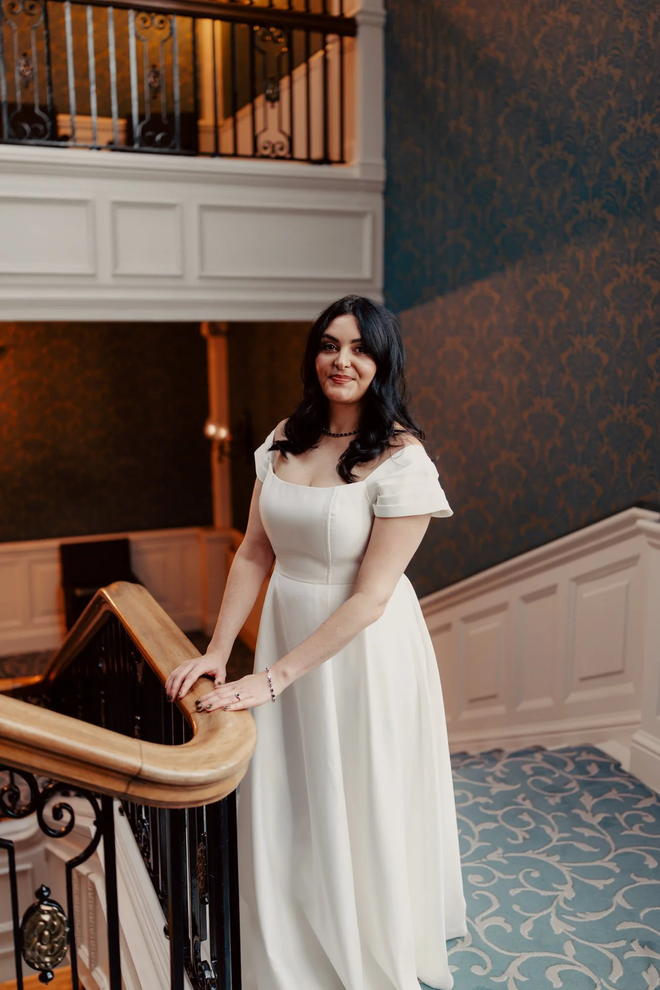 Milly beside the curved wooden stair rail in her wedding dress.