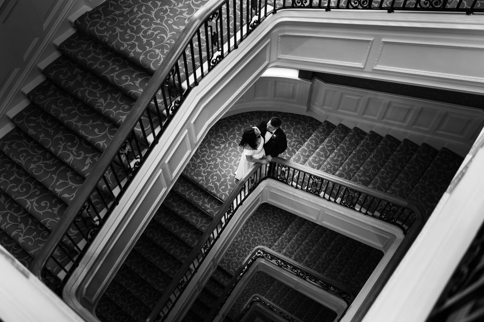 Black-and-white overhead view of the couple on the hotel staircase.