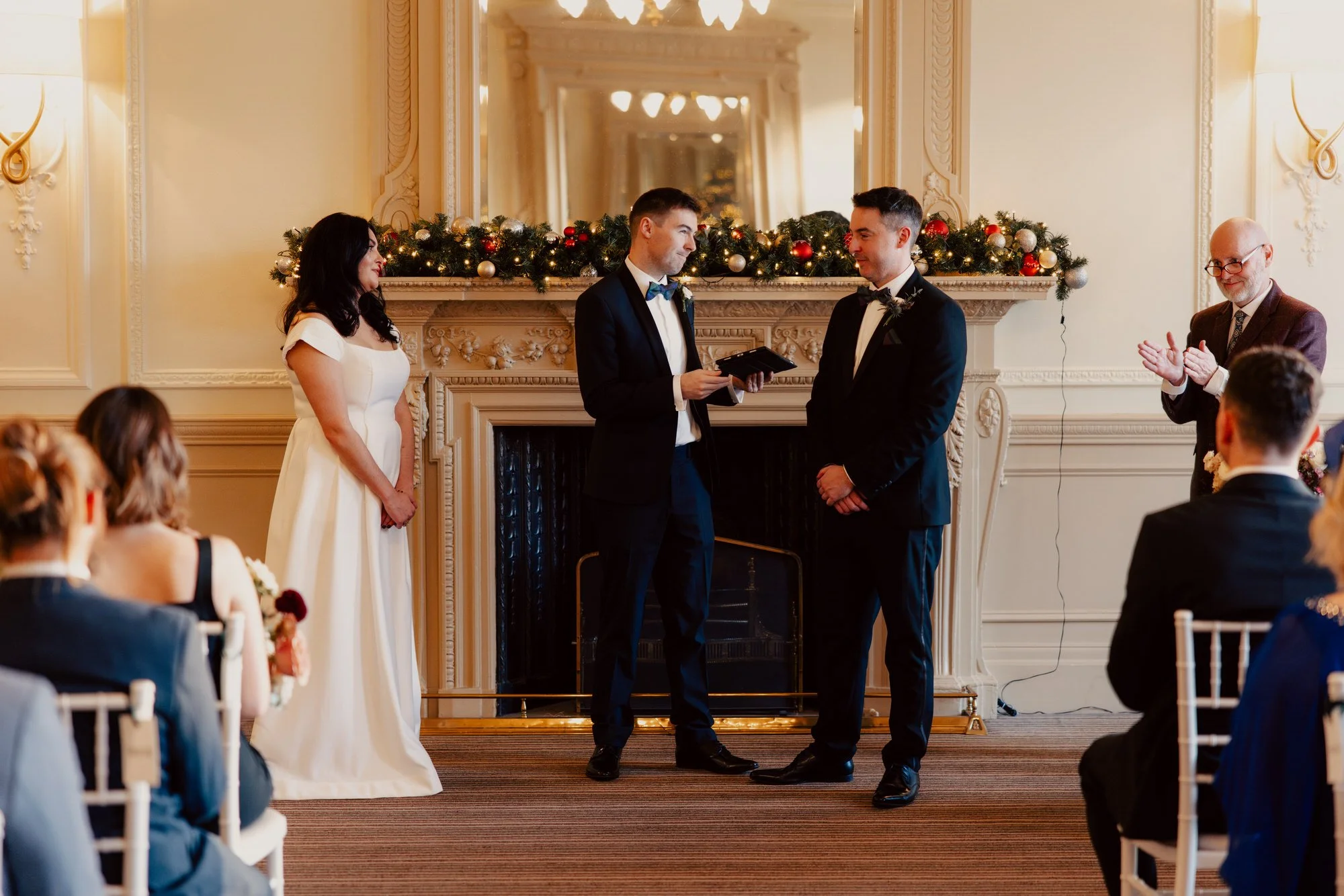 The couple standing with Alan Ness in front of the decorated fireplace.
