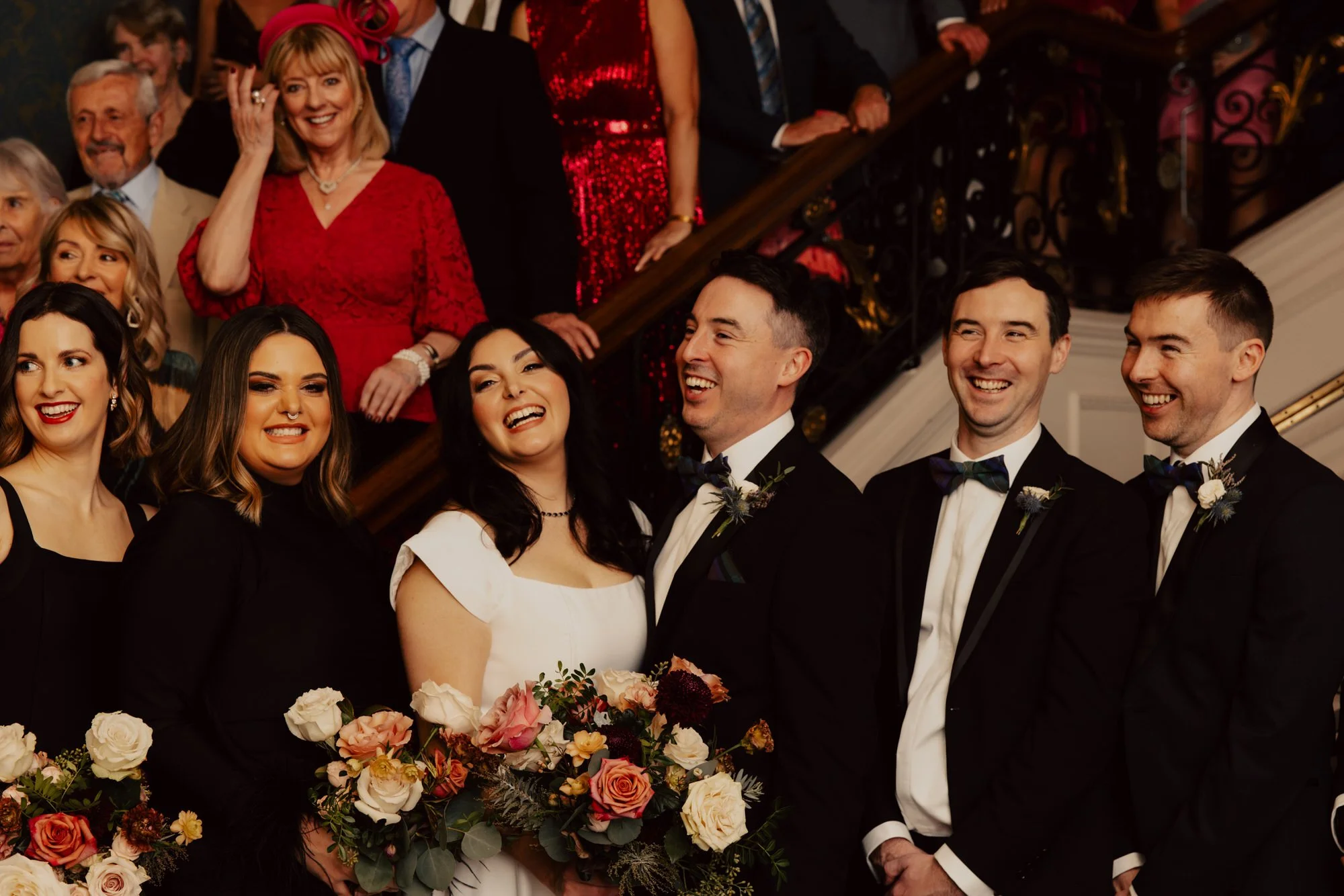 The couple surrounded by smiling friends on the staircase.