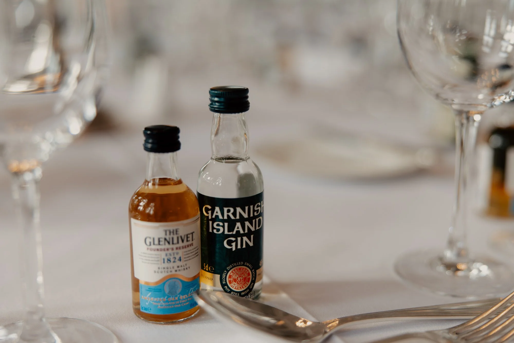 Miniature drinks bottles beside glassware on a wedding table.