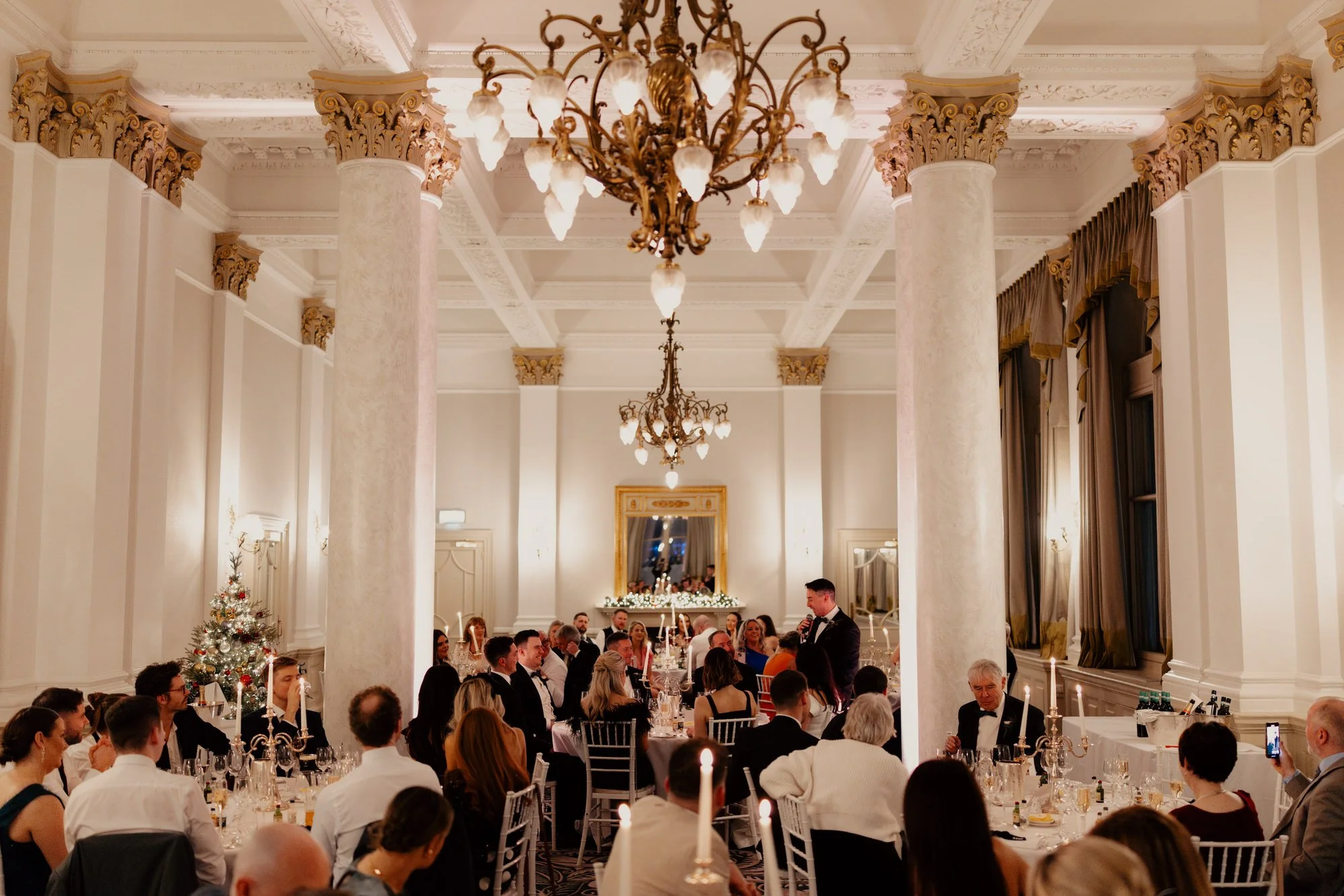 Wide view of guests seated beneath chandeliers for the wedding breakfast.