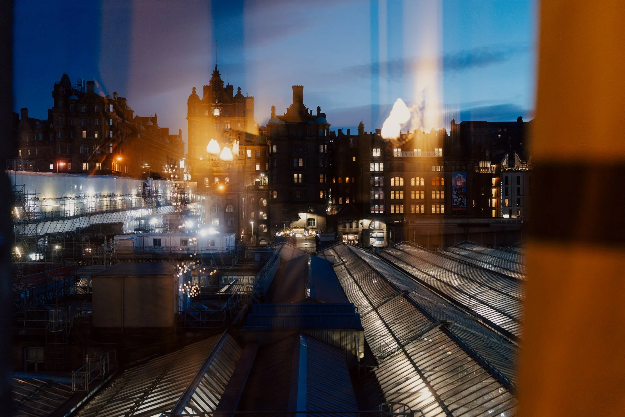 Edinburgh buildings and lights reflected in a hotel window at dusk.