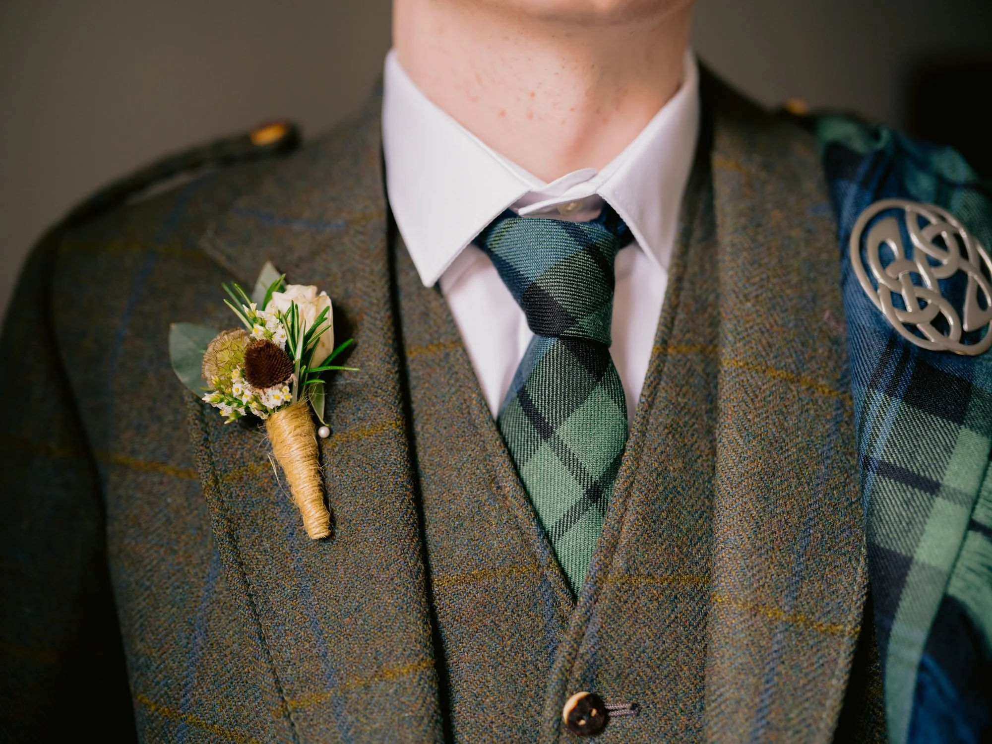 Close-up of the groom’s tartan tie and floral buttonhole