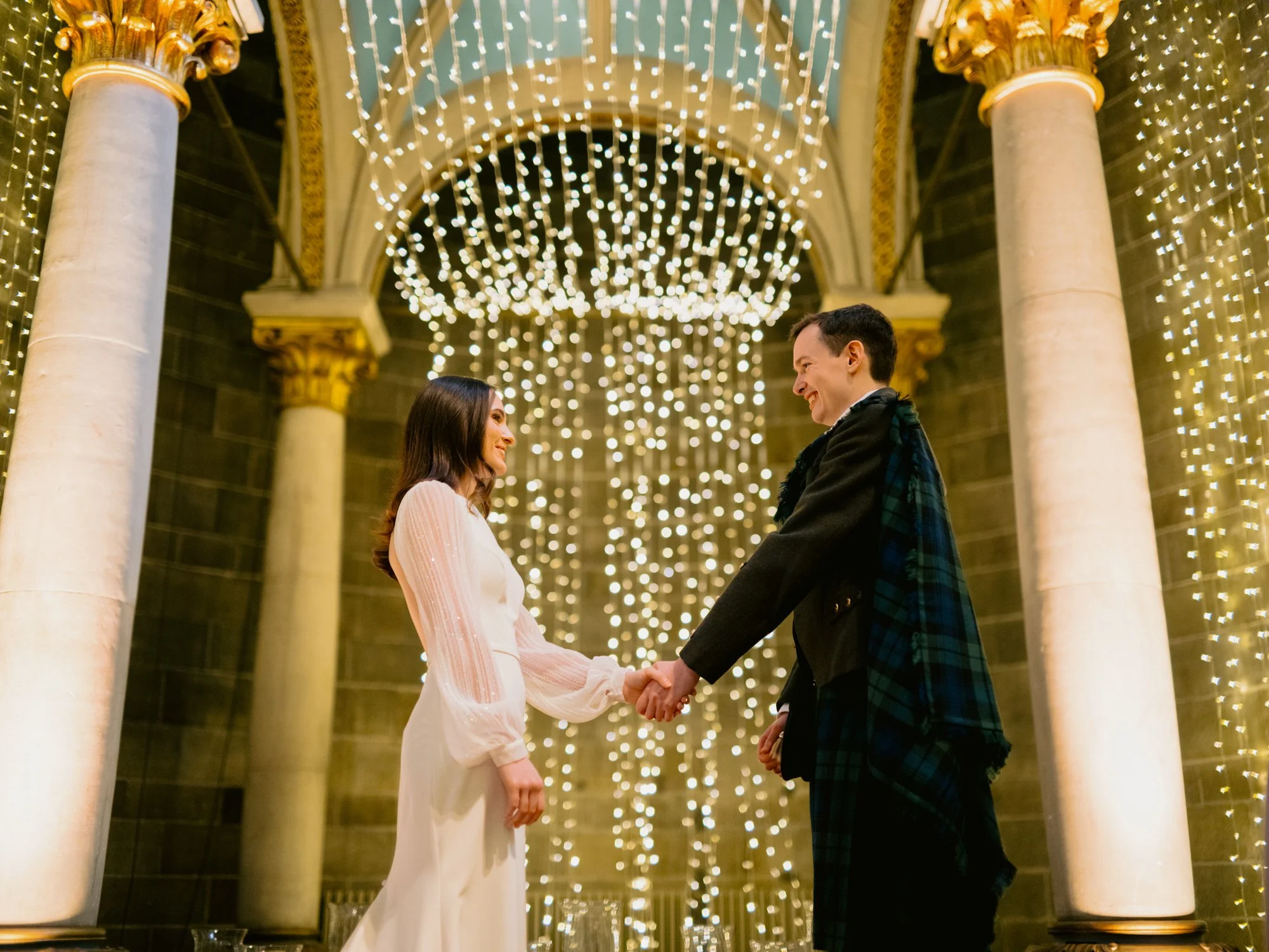 Nicola and Fraser holding hands beneath strings of lights
