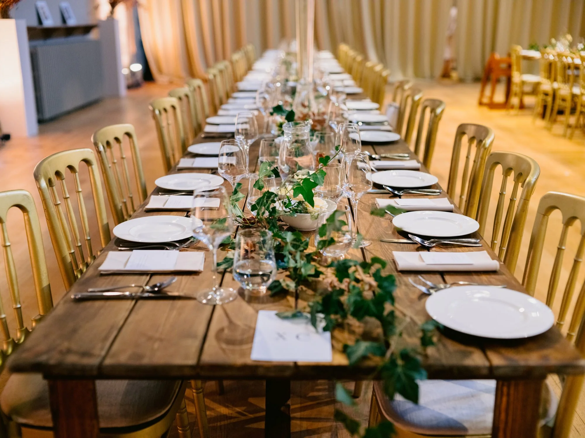 Long wooden wedding table set with gold chairs and flowers