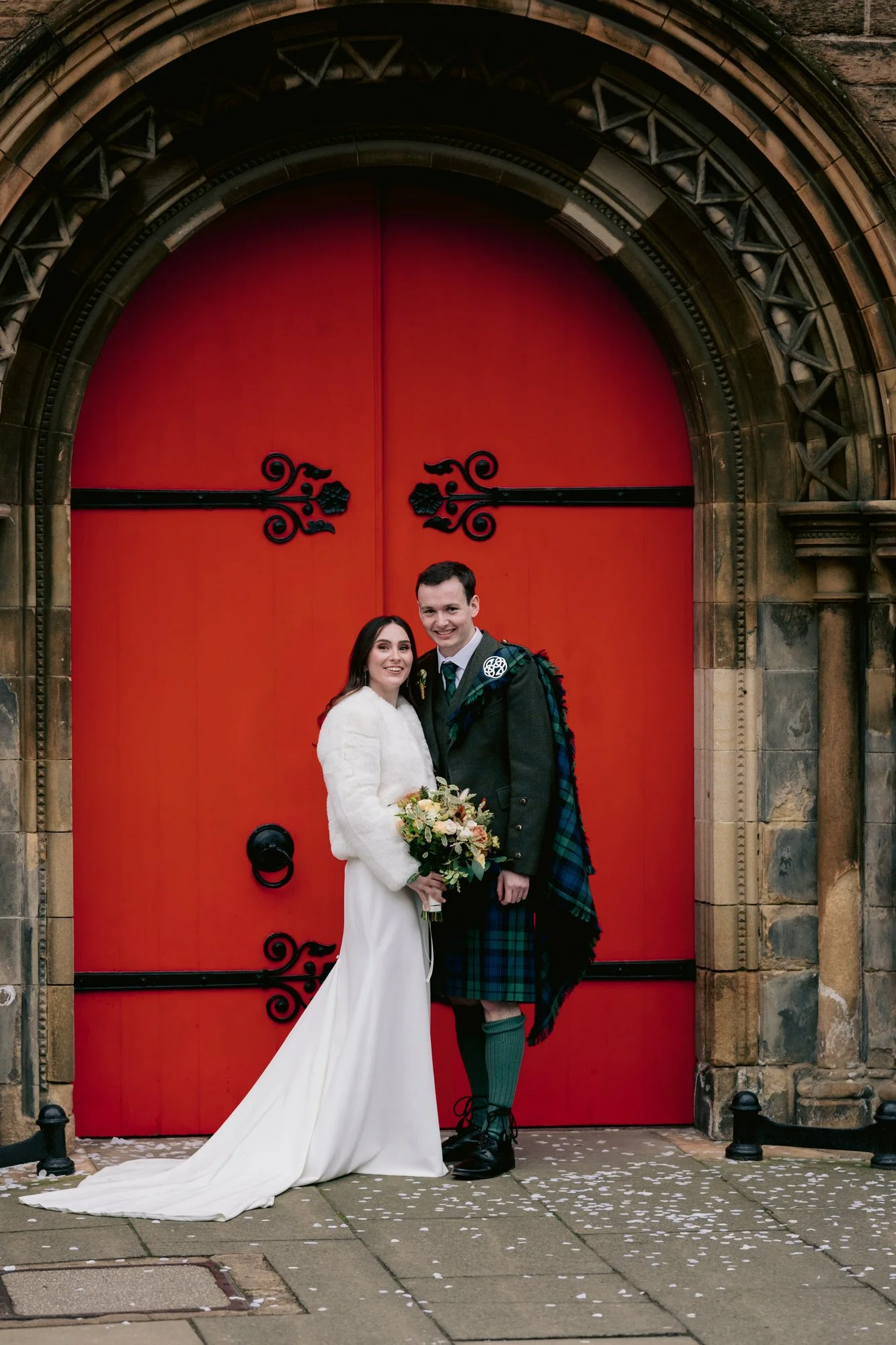 Nicola and Fraser standing in front of Mansfield Traquair’s red doors