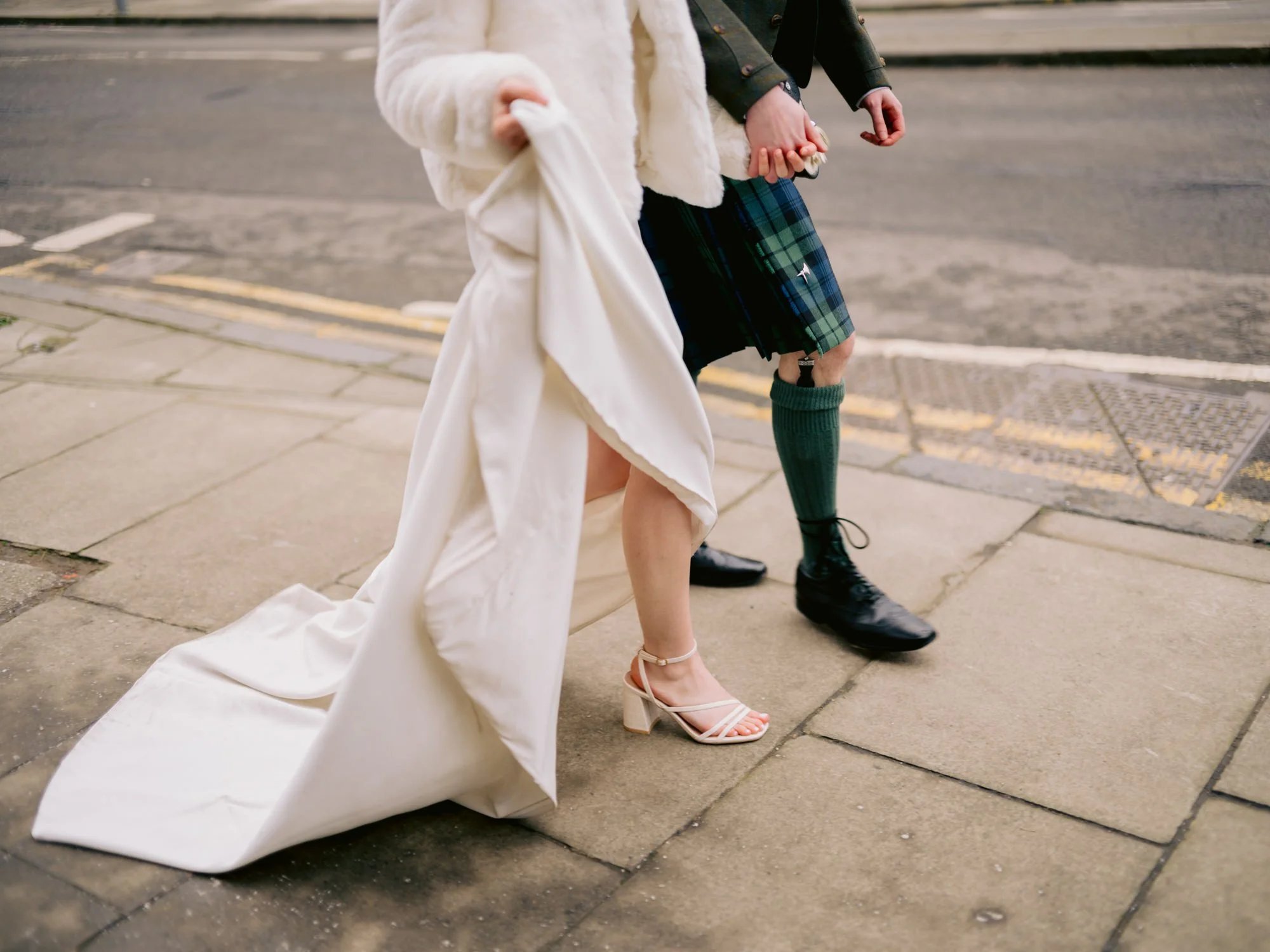 Close-up of the bride’s shoes and groom’s kilt as they walk