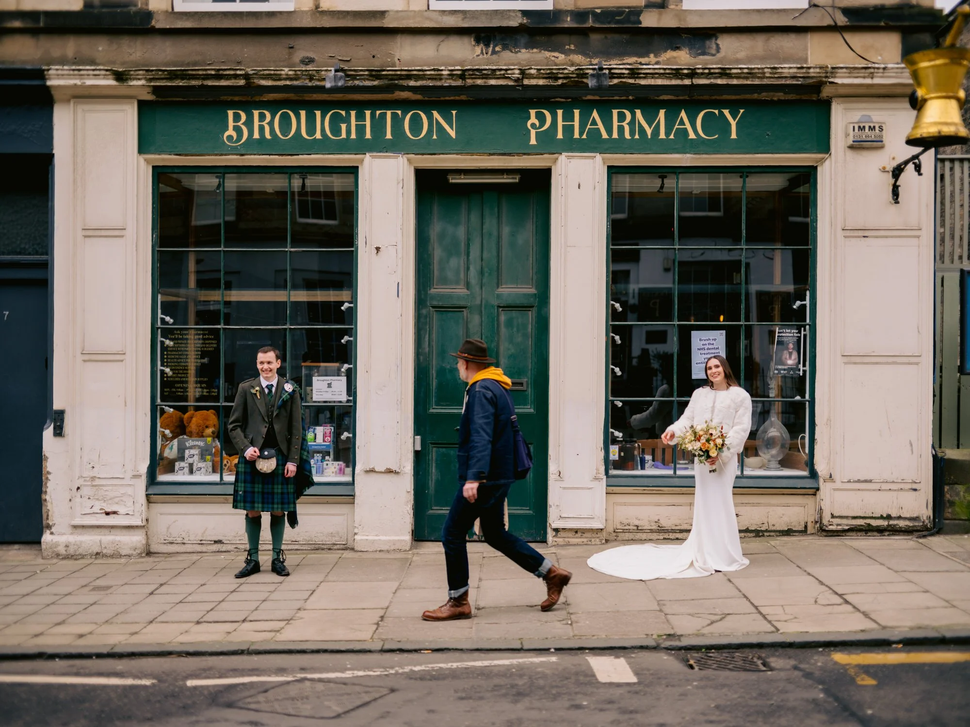 The couple passing the green frontage of Broughton Pharmacy